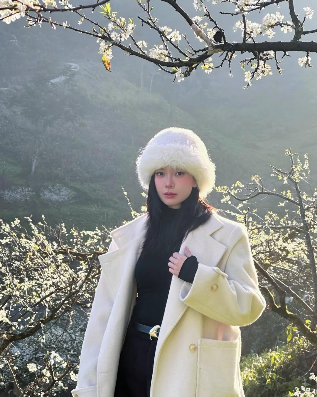 Giữa khung cảnh thiên nhiên mờ sương, những cành mận trắng muốt bung nở khắp triền đồi, Đỗ Yên Đan xuất hiện với phong cách nhẹ nhàng, tinh tế, tạo nên tổng thể hài hòa và đầy chất thơ.