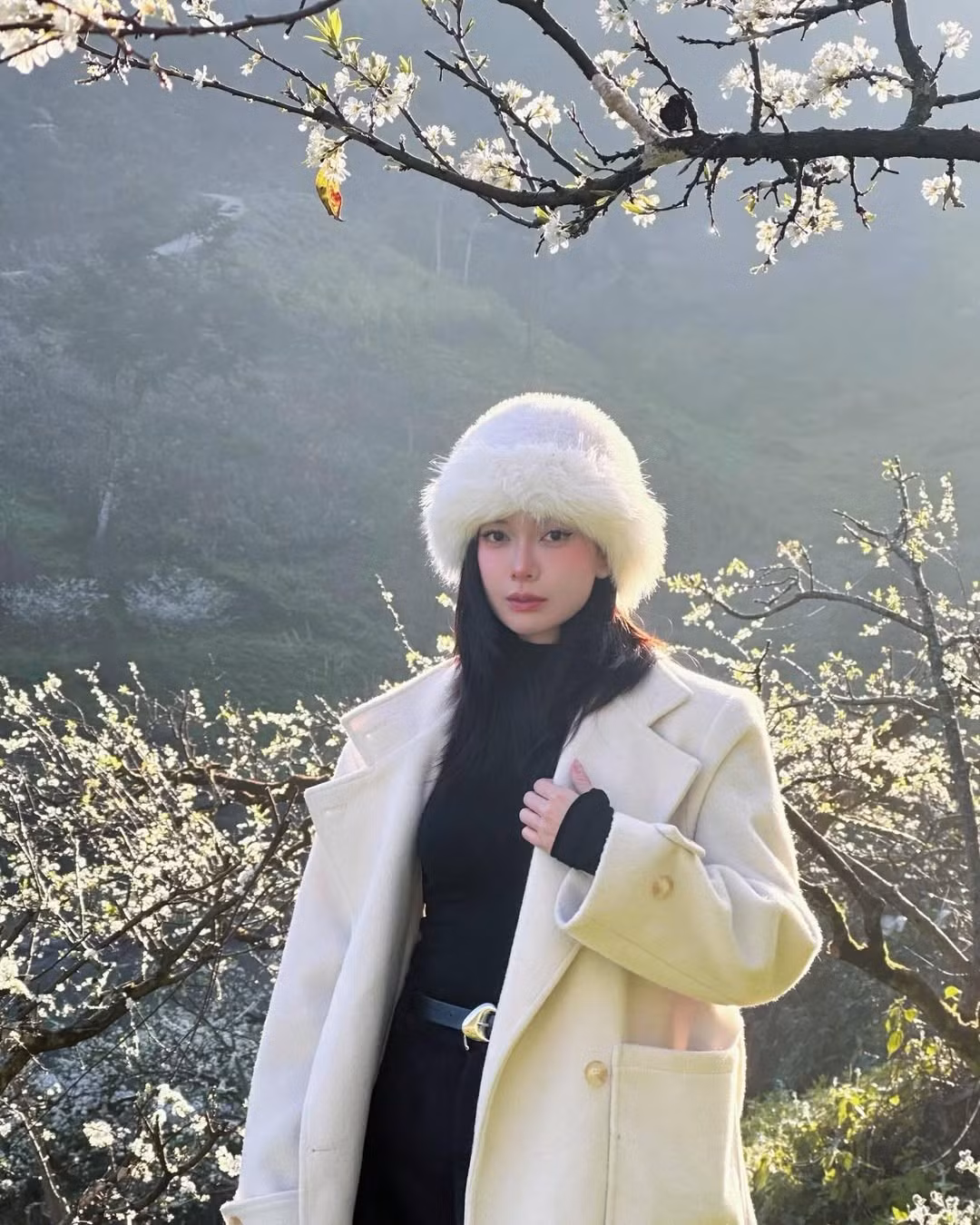 Giữa khung cảnh thiên nhiên mờ sương, những cành mận trắng muốt bung nở khắp triền đồi, Đỗ Yên Đan xuất hiện với phong cách nhẹ nhàng, tinh tế, tạo nên tổng thể hài hòa và đầy chất thơ.