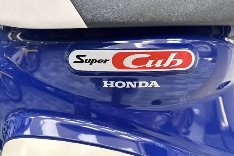 Phần đầu xe không còn kiểu bo tròn cổ điển mà được kéo dài, tích hợp giá đỡ và rổ kim loại cỡ lớn phía trước, phục vụ chở hàng. Đèn pha đặt thấp, tách biệt khỏi tay lái – một bố cục hiếm gặp trên các dòng Cub dân dụng. Cụm đồng hồ analog nay có thêm màn hình nhỏ chỉ báo đa thông tin và đèn báo ABS., các phím bấm thiết kế đơn giản, dễ sử dụng...