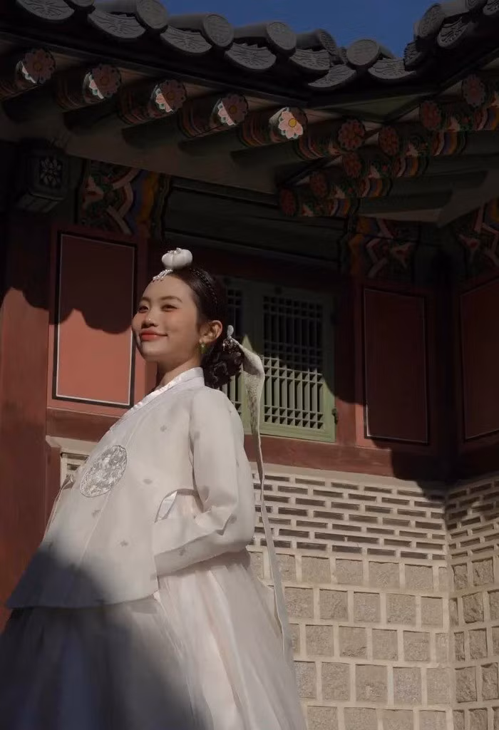 Cô chọn một bộ Hanbok truyền thống mang tông màu trắng kem tinh khôi, vô cùng thanh lịch. Thiết kế có nhiều lớp vải voan mỏng, bồng bềnh, cùng các chi tiết hoa văn thêu chìm tinh xảo trên thân váy và áo