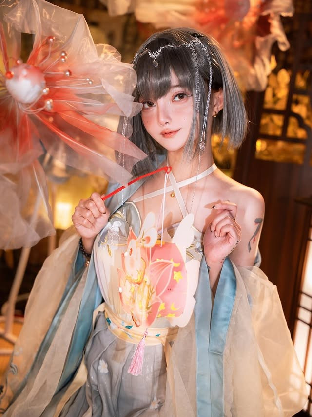 Trong bộ ảnh này, "búp bê" của giới cosplay Le Josette hóa thân thành một nàng tiên dịu dàng trong khung cảnh đậm chất Á Đông, ánh đèn lồng vàng cam và sắc lụa mờ ảo tạo nên bầu không khí vừa cổ điển vừa huyền ảo.