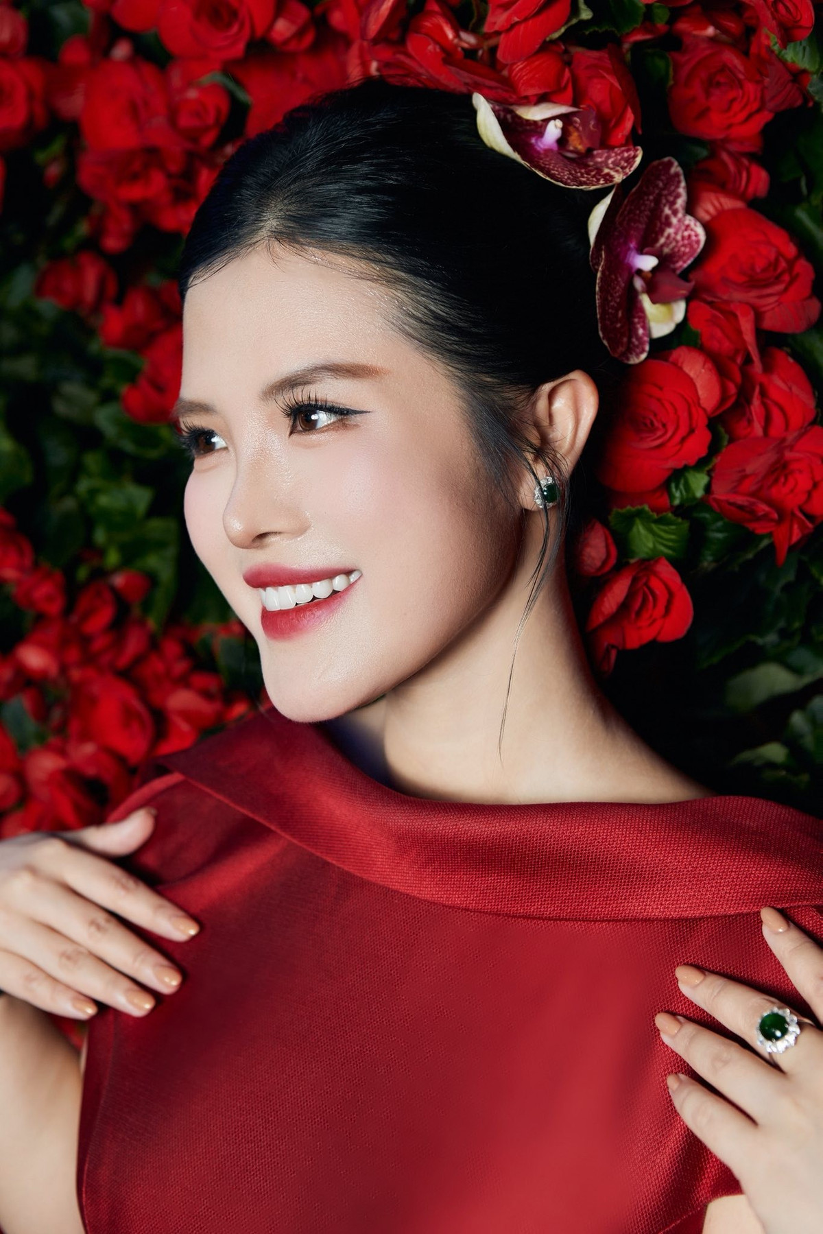 Ở góc chụp cận mặt, các đường nét thanh tú càng trở nên rõ ràng: sống mũi cao, nụ cười rạng rỡ, ánh mắt long lanh – tất cả tạo nên visual kiêu sa, đậm chất minh tinh. Hình ảnh Hải Vân nổi bật giữa phông nền hoa đỏ tựa như một đóa hoa nở rộ, thu hút ánh nhìn từ mọi ống kính.