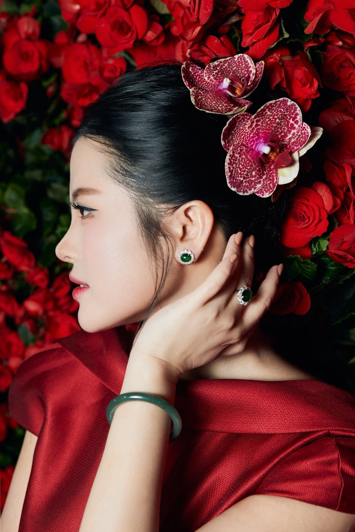 Gương mặt của Hải Vân càng gây ấn tượng mạnh khi được trang điểm theo phong cách tinh tế: làn da mịn màng tươi sáng, đôi mắt sâu cuốn hút với eyeliner sắc nét, hàng mi cong vút, cùng bờ môi đỏ nhung nổi bật. Mái tóc búi cao gọn gàng kết hợp điểm nhấn bằng những bông lan đỏ cài duyên dáng phía sau tạo nên vẻ đẹp vừa Á Đông, vừa quý phái.