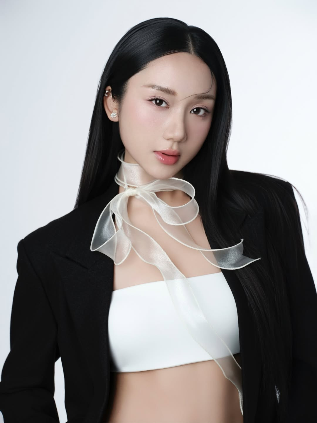 Trong bộ ảnh mới, Mina Young xuất hiện với concept tối giản nhưng đầy tính thời trang. Cô lựa chọn blazer đen dáng rộng phối cùng áo crop top trắng, kết hợp chân váy ngắn và tất mỏng, tạo nên tổng thể vừa thanh lịch vừa gợi cảm một cách tinh tế. Điểm nhấn đặc biệt nằm ở chiếc nơ lụa mỏng buộc hờ quanh cổ, bay nhẹ theo từng chuyển động, mang lại cảm giác mềm mại và đầy chất thơ giữa phông nền studio đơn sắc.