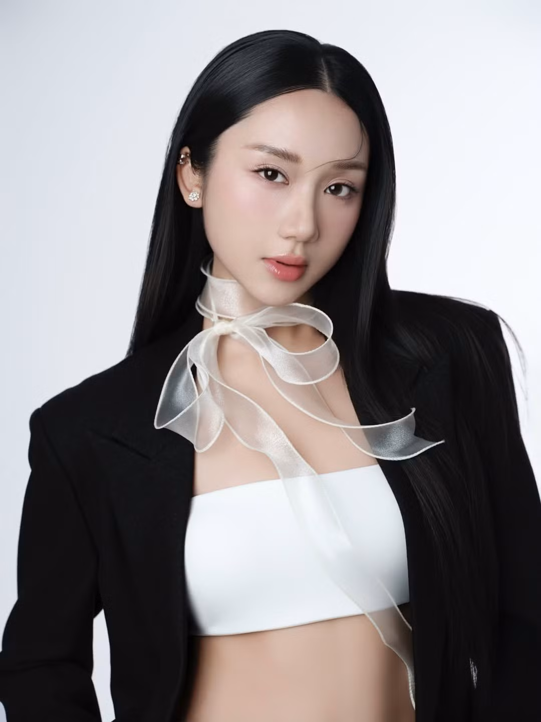 Trong bộ ảnh mới, Mina Young xuất hiện với concept tối giản nhưng đầy tính thời trang. Cô lựa chọn blazer đen dáng rộng phối cùng áo crop top trắng, kết hợp chân váy ngắn và tất mỏng, tạo nên tổng thể vừa thanh lịch vừa gợi cảm một cách tinh tế. Điểm nhấn đặc biệt nằm ở chiếc nơ lụa mỏng buộc hờ quanh cổ, bay nhẹ theo từng chuyển động, mang lại cảm giác mềm mại và đầy chất thơ giữa phông nền studio đơn sắc.