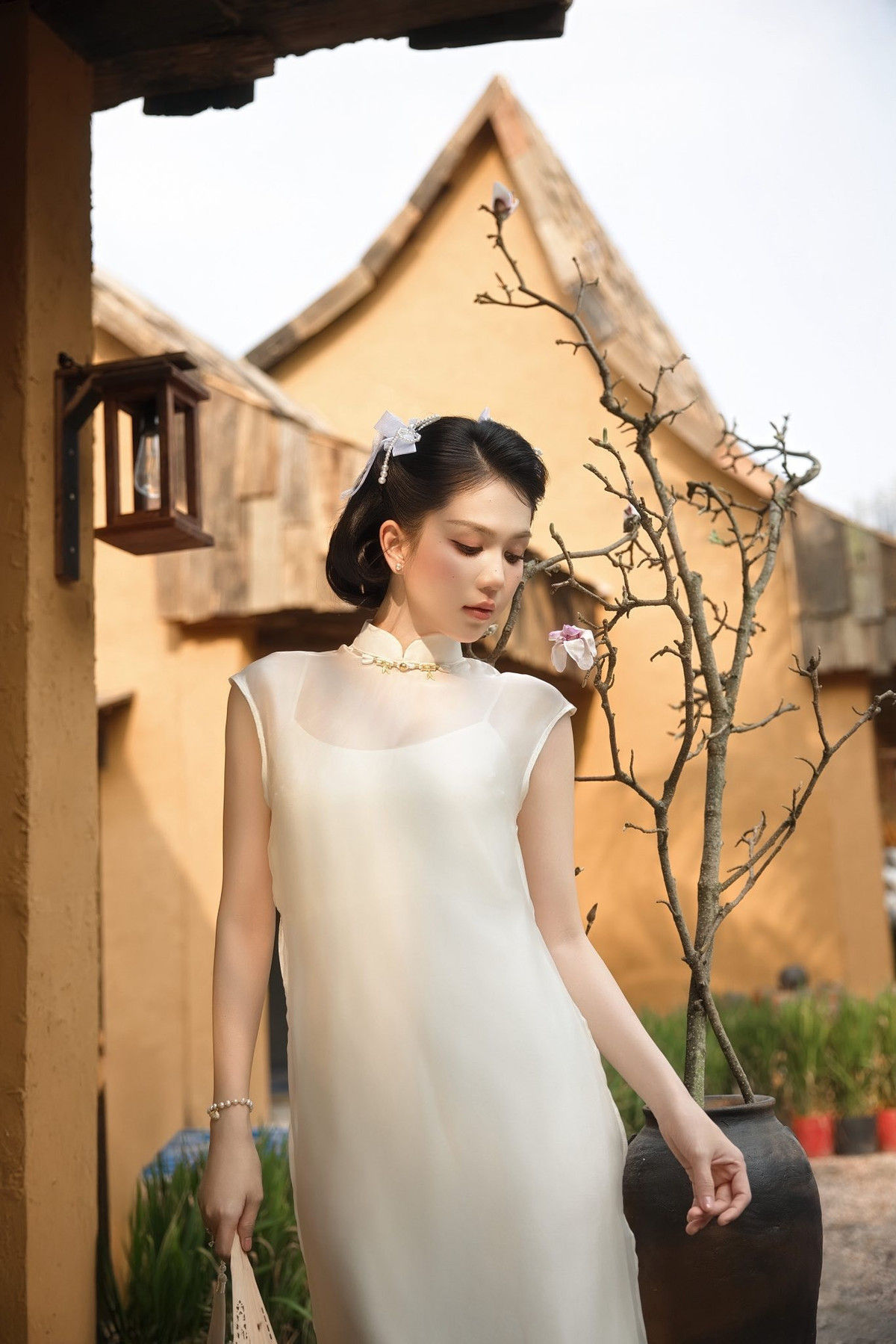 Lựa chọn trang phục là một thiết kế áo dài cách tân màu trắng ngà, Ngọc Trinh ghi điểm với vẻ ngoài thuần khiết và thanh lịch. Phom dáng suông mềm mại, phần cổ cao và lớp voan mỏng phủ nhẹ phía trên giúp tổng thể vừa giữ được nét truyền thống của áo dài, vừa mang hơi thở hiện đại. Chất liệu bay nhẹ theo từng bước đi càng làm nổi bật vẻ nữ tính, dịu dàng của người mặc.