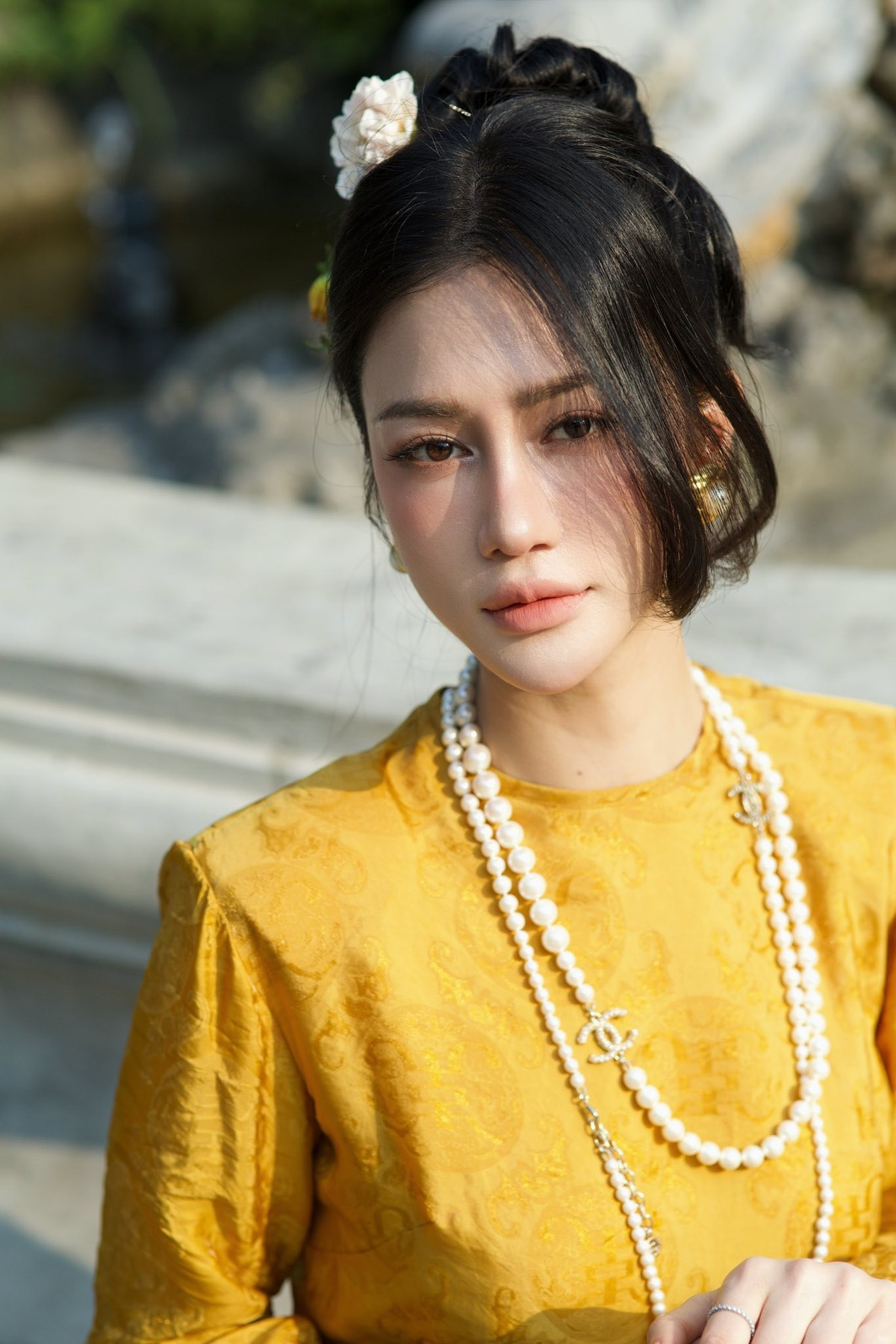 Trong loạt ảnh được thực hiện tại không gian mang hơi thở kiến trúc cổ điển, Trần Ngọc Bích lựa chọn áo dài gam vàng ấm, chất liệu gấm nhẹ, tôn lên nét quý phái.