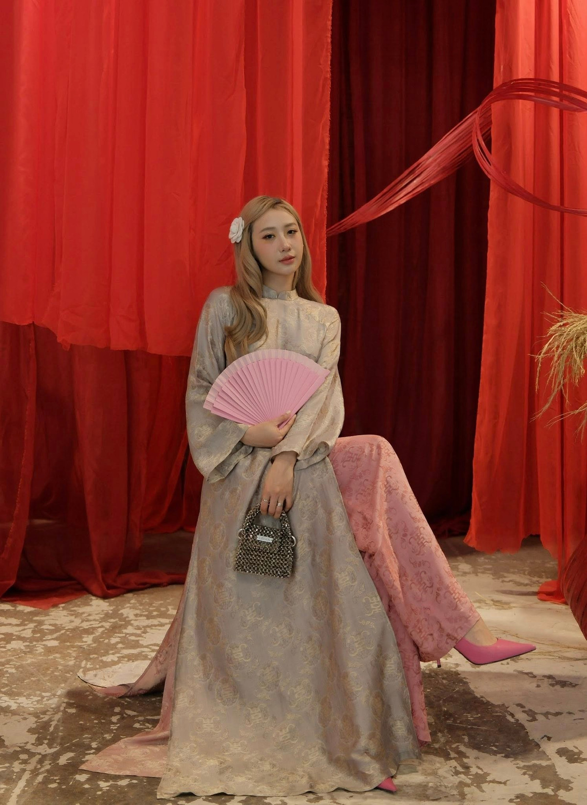 Điểm đặc biệt của bộ trang phục nằm ở chất liệu gấm cao cấp, bắt sáng nhẹ, tạo hiệu ứng thị giác sang trọng dưới ánh đèn studio. Phom dáng áo dài truyền thống được giữ nguyên với cổ cao kín đáo, nhưng được tiết chế chi tiết để tôn lên vóc dáng thanh mảnh của người mặc. Nhờ vậy, hình ảnh “hot mom” không chỉ gợi cảm mà còn toát lên vẻ quý phái, nền nã rất Á Đông.