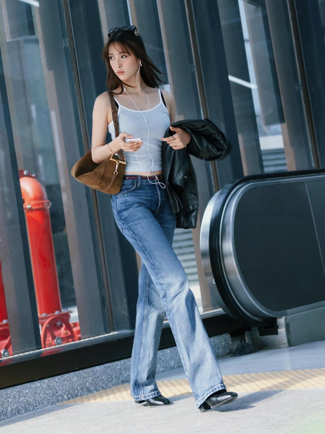 Trong loạt ảnh, Trần Tiểu Vy xuất hiện với set đồ street style năng động gồm áo hai dây dáng ôm tôn vòng eo thon gọn, quần jeans ống suông trẻ trung, phối cùng túi xách và áo khoác da khoác tay. Tai nghe trắng, kính mát cài đầu và mái tóc dài bay nhẹ trong gió tạo nên tổng thể vừa hiện đại, vừa phóng khoáng. Phong cách đời thường giản dị nhưng lại giúp nàng hậu khoe trọn vóc dáng cân đối cùng thần thái tự tin khi sải bước giữa không gian đô thị.