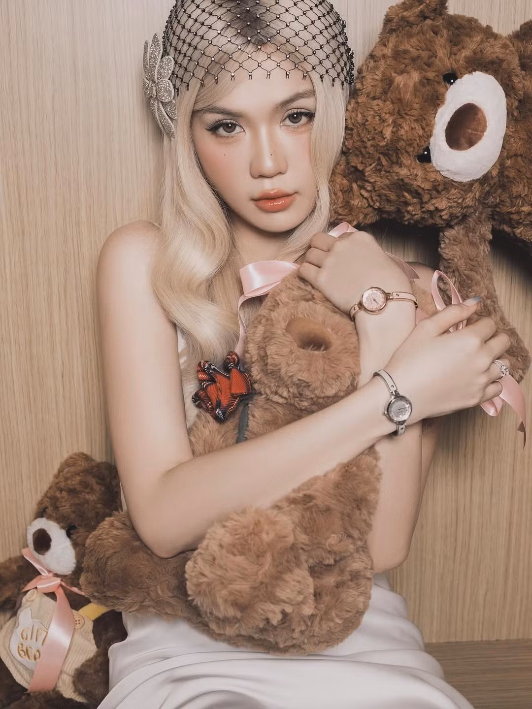 Điểm nhấn đáng chú ý nhất chính là mái tóc vàng bạch kim buông xoã, uốn sóng nhẹ mang hơi hướng retro, kết hợp cùng mạng che đầu đính đá độc đáo. Phụ kiện đặc biệt này khiến diện mạo của cô trở nên khác lạ, đầy tính thời trang và mang nét cổ điển quý phái.