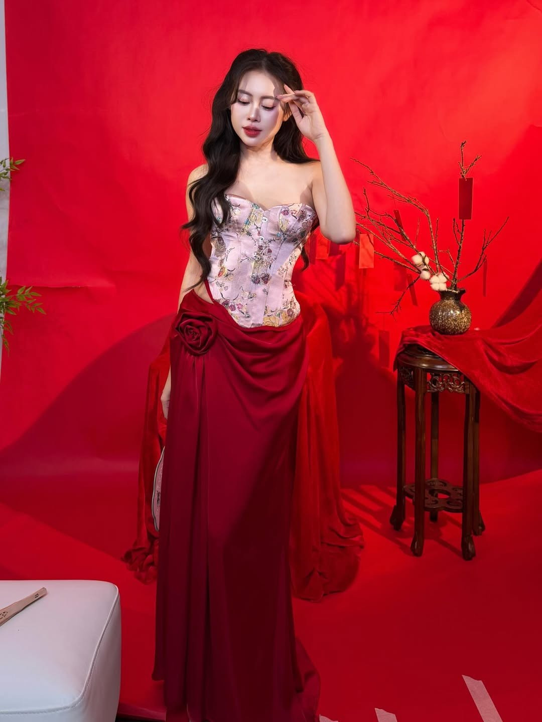 Trong bộ ảnh đón xuân, Việt Phương Thoa lựa chọn phong cách gợi cảm pha nét truyền thống. Thiết kế corset thêu hoa kết hợp chân váy đỏ rực giúp tôn lên đường cong cơ thể, đồng thời hòa cùng sắc đỏ đặc trưng của ngày Tết. Phông nền đơn sắc cùng các đạo cụ như cành lộc, phong bao lì xì tạo nên bầu không khí xuân rộn ràng nhưng vẫn giữ được tinh thần thời trang hiện đại.