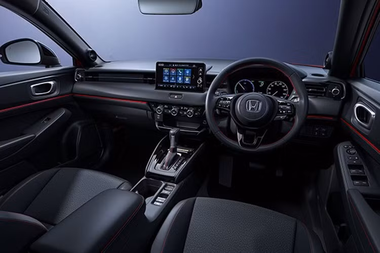 Khoang nội thất của Honda HR-V e:HEV RS 2026 mới vẫn tiếp tục trung thành với phong cách RS: tông đen chủ đạo, chỉ khâu đỏ tương phản, vô lăng bọc da thật và ghế da lộn tạo cảm giác thể thao, cao cấp.