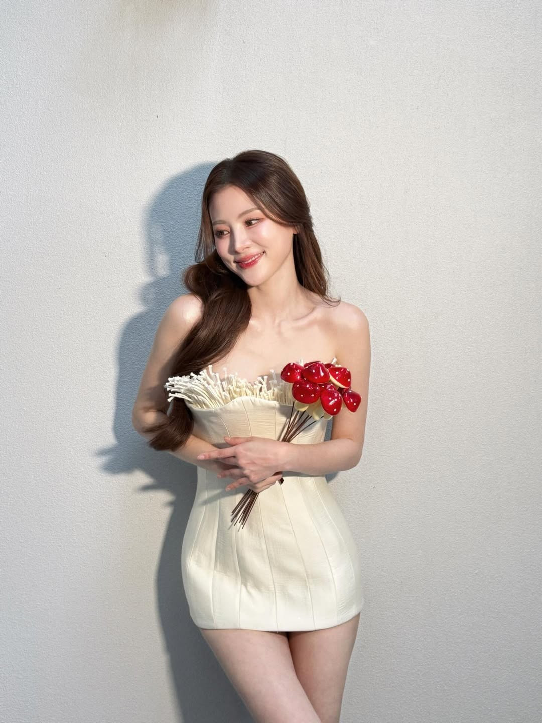 Trong bộ ảnh, Baifern diện mẫu váy dáng cúp ngực tông trắng – kem chủ đạo, ôm sát vòng eo thon gọn và tôn trọn vóc dáng mảnh mai. Điểm nhấn đặc biệt nằm ở phần thân trên của váy với những chi tiết tua mềm, xòe nhẹ, được xử lý tinh tế như những sợi nấm mảnh vươn lên, tạo hiệu ứng thị giác vừa lạ mắt vừa nghệ thuật.