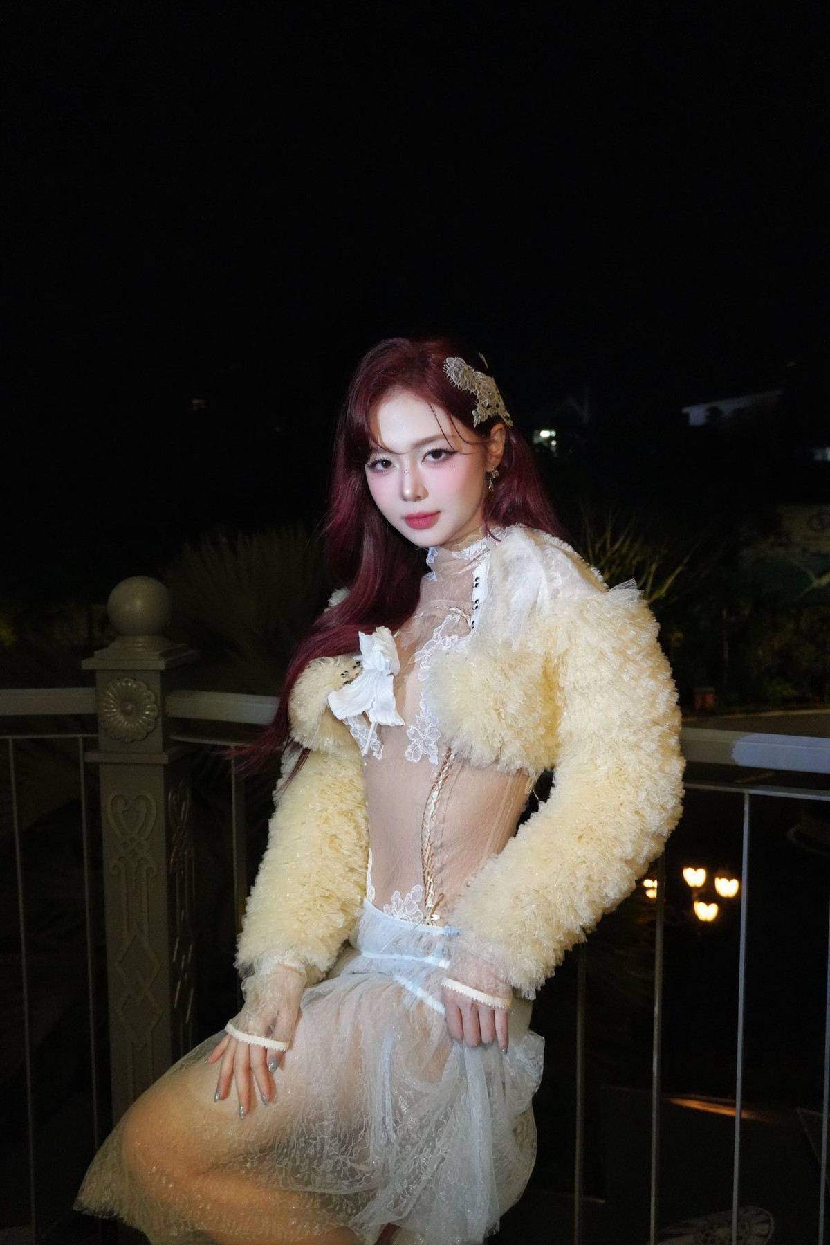 Trong khung cảnh đêm, ánh đèn chiếu nhẹ lên gương mặt Liz Kim Cương càng làm nổi bật làn da sáng mịn và đường nét hài hòa. Gương mặt nhỏ nhắn, sống mũi thon, đôi mắt sắc nhưng ngọt ngào, cùng lớp trang điểm tinh tế giúp cô trông như một nàng thơ mang vẻ đẹp hiện đại. Mái tóc đỏ trầm buông xoã tạo điểm nhấn bắt mắt, ton-sur-ton hoàn hảo với phong cách quyến rũ mà cô theo đuổi.