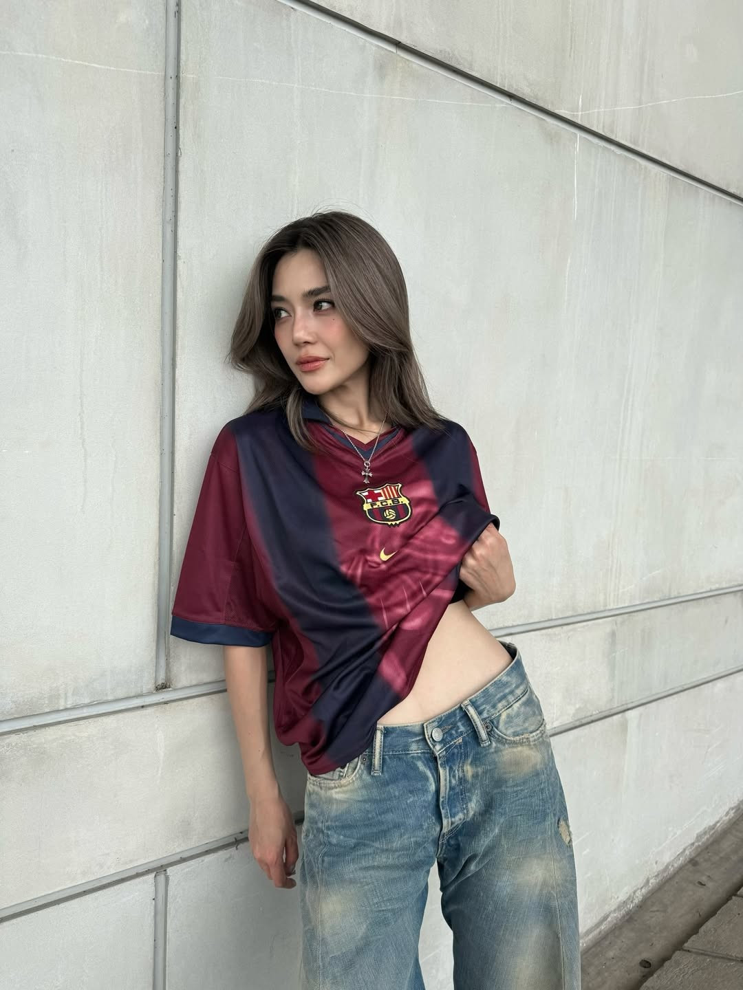 Trong những khung hình được chia sẻ, Prang Kannarun lựa chọn áo đấu Barca form rộng, buộc gọn phần gấu áo để khéo léo khoe vòng hai phẳng lì. Cô phối cùng quần jeans ống suông bụi bặm, sneakers trắng và trang sức tối giản, tạo nên tổng thể street style vừa cá tính vừa gợi cảm.