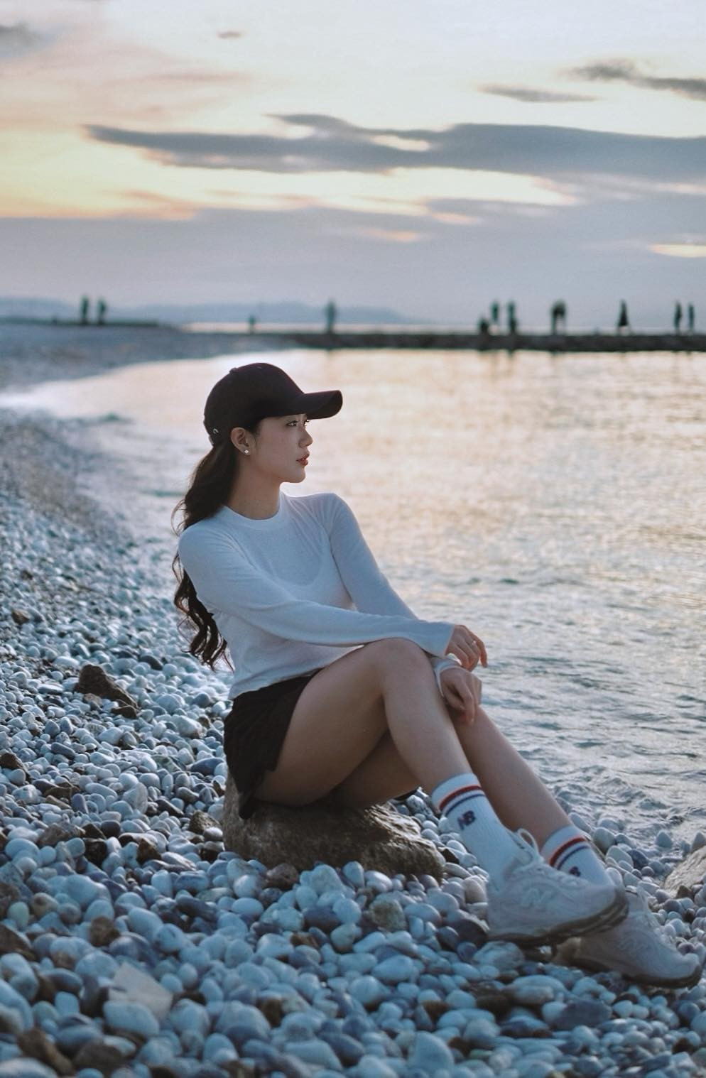 Giữa khung cảnh biển xanh, bờ sỏi trải dài và ánh hoàng hôn dịu nhẹ, Tôn Nữ Nam Phương lựa chọn phong cách trẻ trung với áo dài tay dáng ôm kết hợp chân váy ngắn, mũ lưỡi trai và giày thể thao. Cách phối đồ đơn giản nhưng tinh tế giúp cô tôn lên sắc vóc thon gọn, đôi chân dài cân đối cùng thần thái khỏe khoắn.