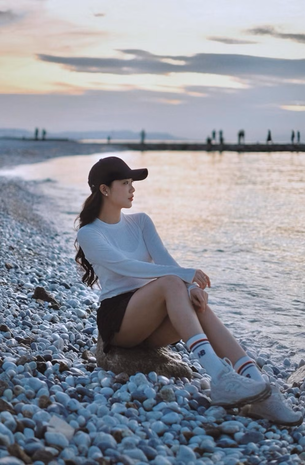 Giữa khung cảnh biển xanh, bờ sỏi trải dài và ánh hoàng hôn dịu nhẹ, Tôn Nữ Nam Phương lựa chọn phong cách trẻ trung với áo dài tay dáng ôm kết hợp chân váy ngắn, mũ lưỡi trai và giày thể thao. Cách phối đồ đơn giản nhưng tinh tế giúp cô tôn lên sắc vóc thon gọn, đôi chân dài cân đối cùng thần thái khỏe khoắn.