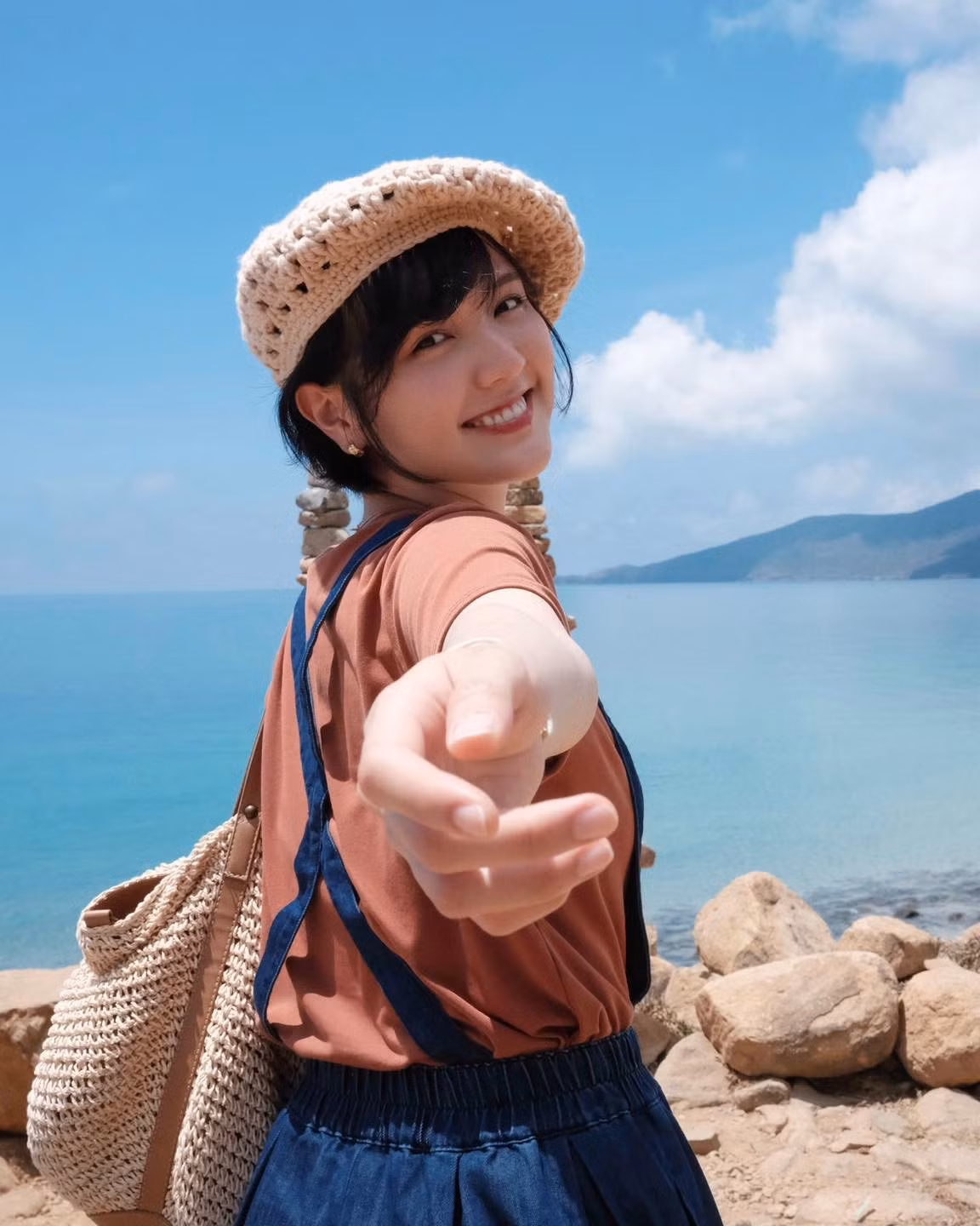 Hải Tú chọn set đồ gồm áo thun cam đất phối cùng quần yếm ống rộng màu xanh navy, đi kèm nón len đan tay và túi tote đan sợi.