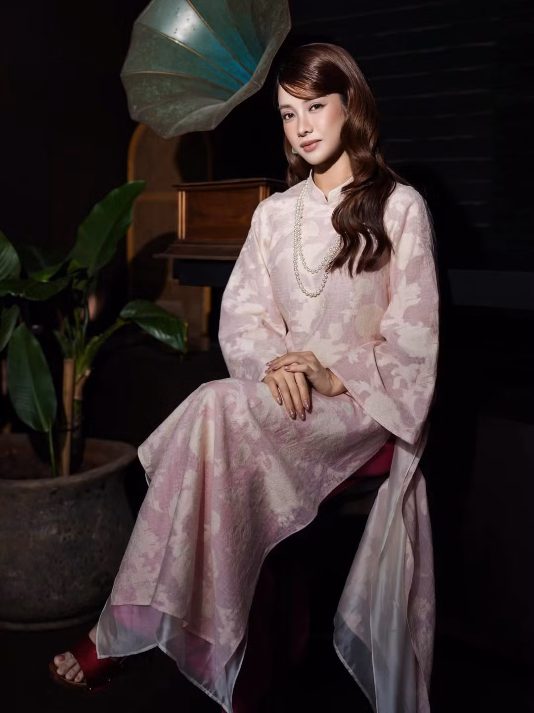 Kiểu tóc uốn nhẹ, rẽ ngôi lệch giúp gương mặt nữ diễn viên thêm phần thanh tú. Cách trang điểm thiên về tông nude, nhấn vào đôi mắt và nụ cười tươi tắn càng làm nổi bật thần thái rạng rỡ. Sự tiết chế trong phụ kiện – chỉ với chuỗi ngọc trai cổ điển – tạo tổng thể hài hòa, sang trọng mà không phô trương.