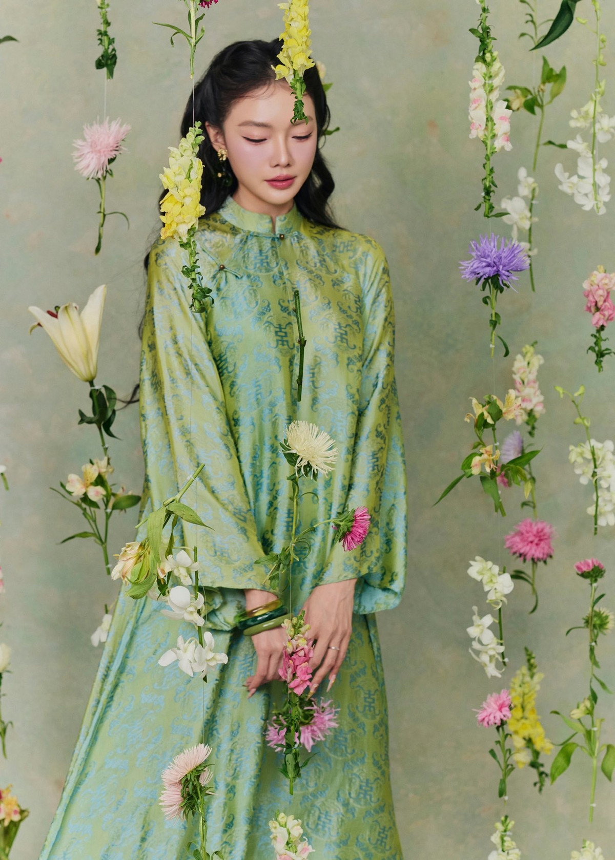 Không gian chụp cũng góp phần tôn lên vẻ đẹp của người mặc. Những dây hoa tươi được sắp đặt rủ xuống từ trên cao, bao quanh người mẫu như một khu vườn treo đầy chất thơ.