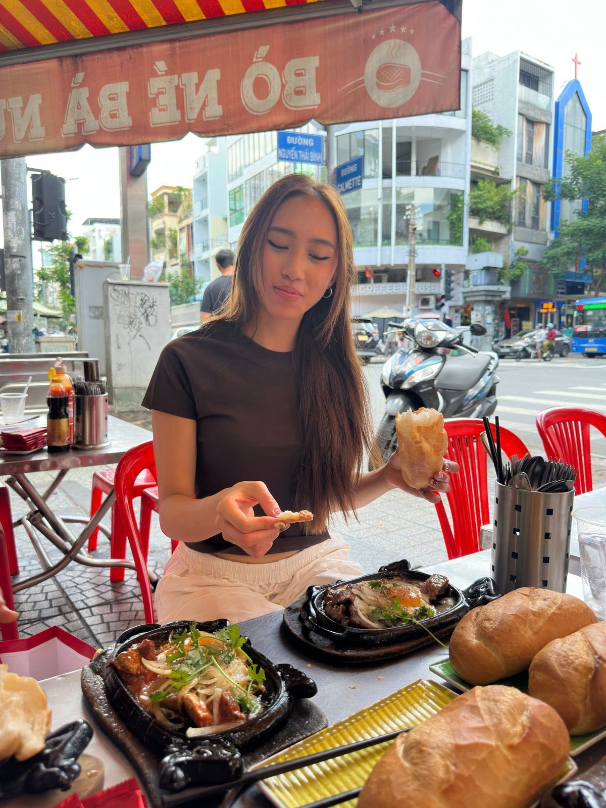 Trong các video được chia sẻ, Tylin tất bật đứng quầy, tay cầm sổ ghi món, miệng tập nói từng câu tiếng Việt còn vấp váp. Có lúc cao điểm, cô vừa nhận đơn, vừa lúng túng tính tiền cho khách, thậm chí đếm nhầm tiền lẻ rồi bật cười ngượng ngùng. Ở góc bếp, cô học cách đập trứng, đặt chảo, nghe tiếng xèo xèo của phần bò né nóng hổi, vừa làm vừa lắng nghe anh chị trong quán chỉ dẫn từng thao tác.