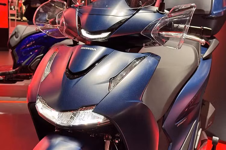 Honda SH125i/150i 2026 được tái thiết kế sâu sắc, lấy cảm hứng từ “đàn anh” SH350i. Phần đầu xe nổi bật với cụm đèn pha LED kép hoàn toàn mới, đi cùng dải đèn định vị sắc nét hơn. Cản trước được tinh chỉnh trở nên mềm mại và khí động học hơn, trong khi từng chi tiết nhỏ như sơn xe, ống xả hay vành đen bóng đều được hoàn thiện tỉ mỉ.