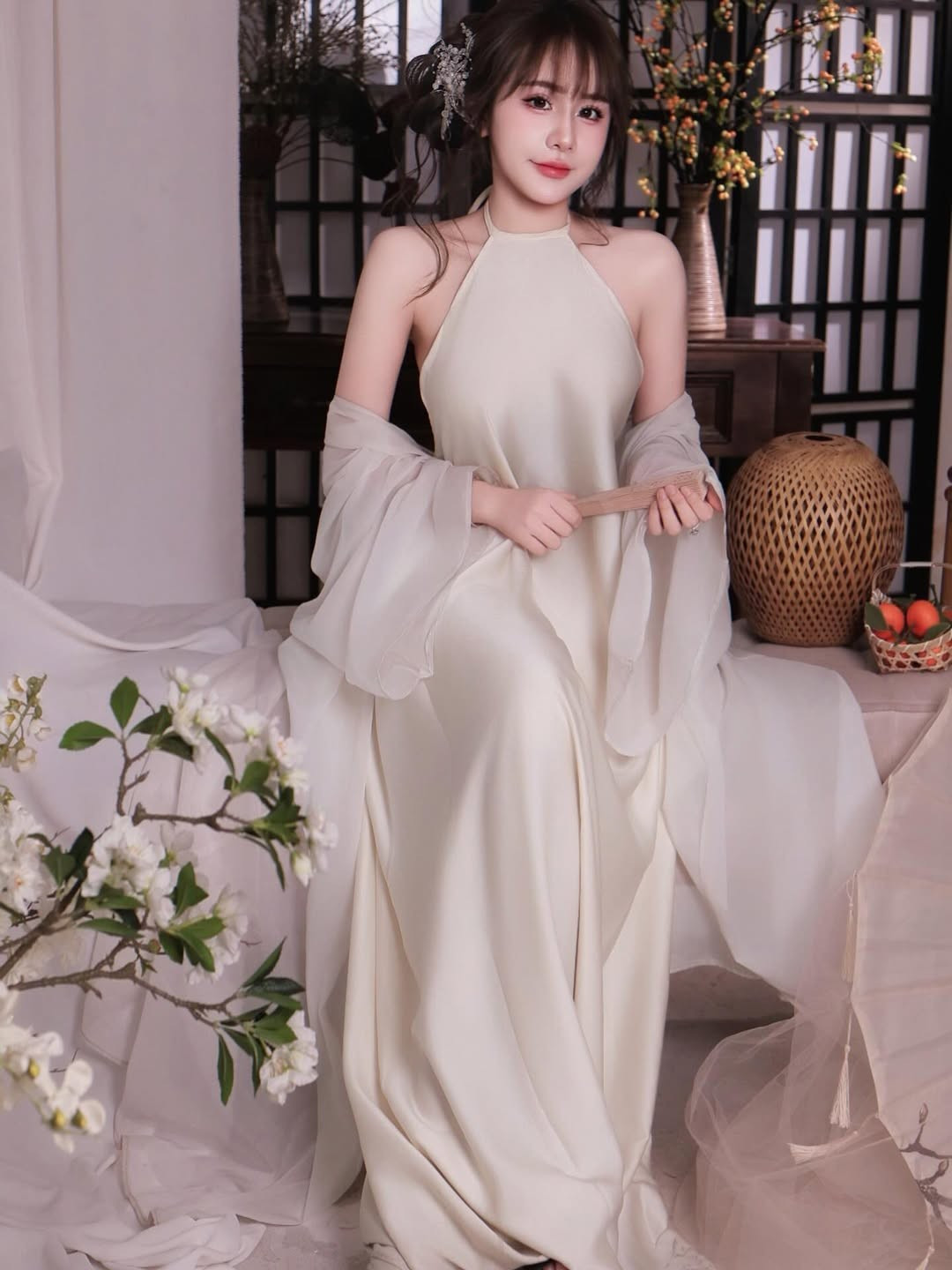 Không gian chụp ảnh cũng góp phần làm nổi bật thần thái của Tuyết Anh. Phông nền mang hơi hướng Á Đông với vách gỗ, bình gốm, cành hoa trắng và ánh sáng dịu nhẹ tạo cảm giác ấm áp, tĩnh lặng.