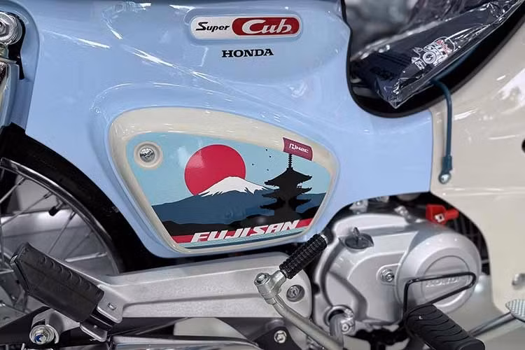 Biểu tượng núi Phú Sĩ, mặt trời mọc trên tem cốp hông xe Honda Super Cub Fujisan. Ngoài ra, các chi tiết như bộ bảo vệ thân xe cùng giá để đồ trước, mang đến vẻ ngoài của chiếc xe số huyền thoại này vừa cổ điển vừa cá tính.