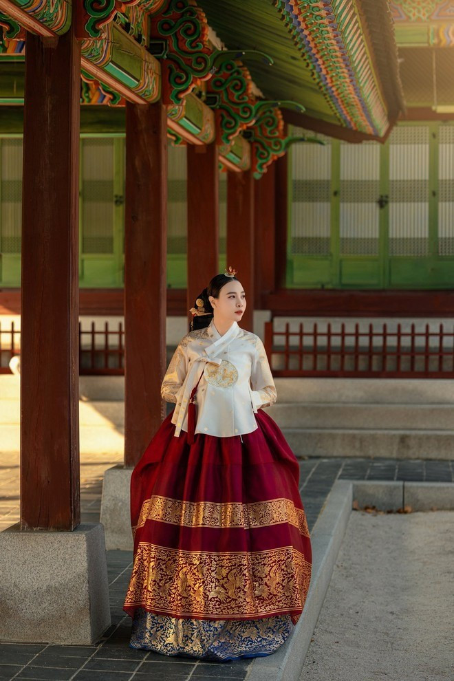 Chiếc áo Jeogori ngắn màu kem nhạt phối cùng váy Chima đỏ rượu xòe bồng, viền đính kim tuyến cầu kỳ ở gấu váy tạo điểm nhấn sang trọng.