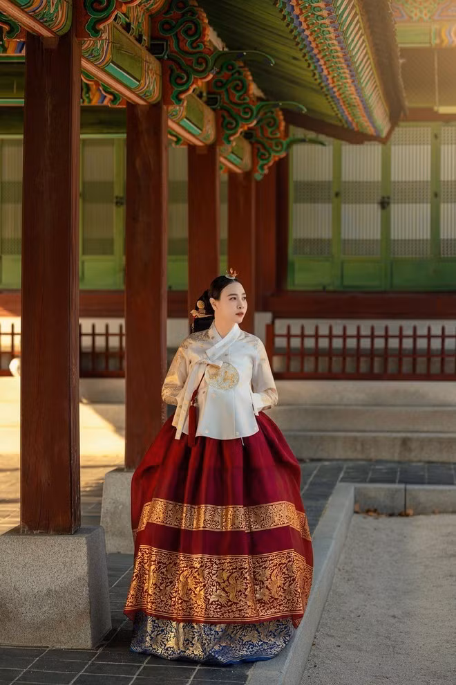 Chiếc áo Jeogori ngắn màu kem nhạt phối cùng váy Chima đỏ rượu xòe bồng, viền đính kim tuyến cầu kỳ ở gấu váy tạo điểm nhấn sang trọng.