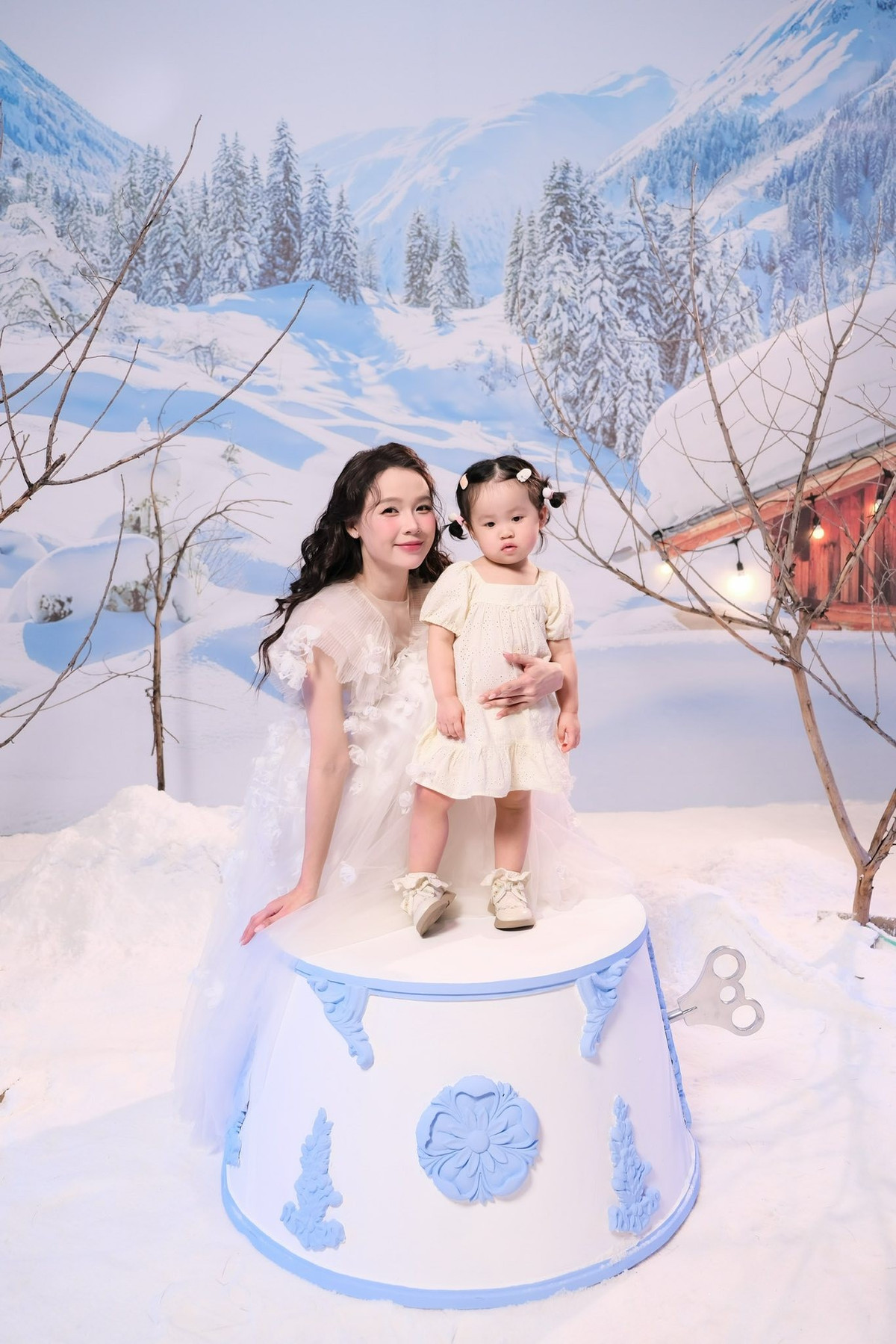 Bên cạnh Sam, con gái nhỏ gây “tan chảy” với vẻ đáng yêu, gương mặt bầu bĩnh, đôi mắt to tròn và những cử chỉ ngây thơ. Sự đồng điệu về màu sắc trang phục và bối cảnh tuyết trắng tạo cảm giác như một câu chuyện cổ tích mùa đông, làm nổi bật tình cảm gia đình hạnh phúc, bình yên.