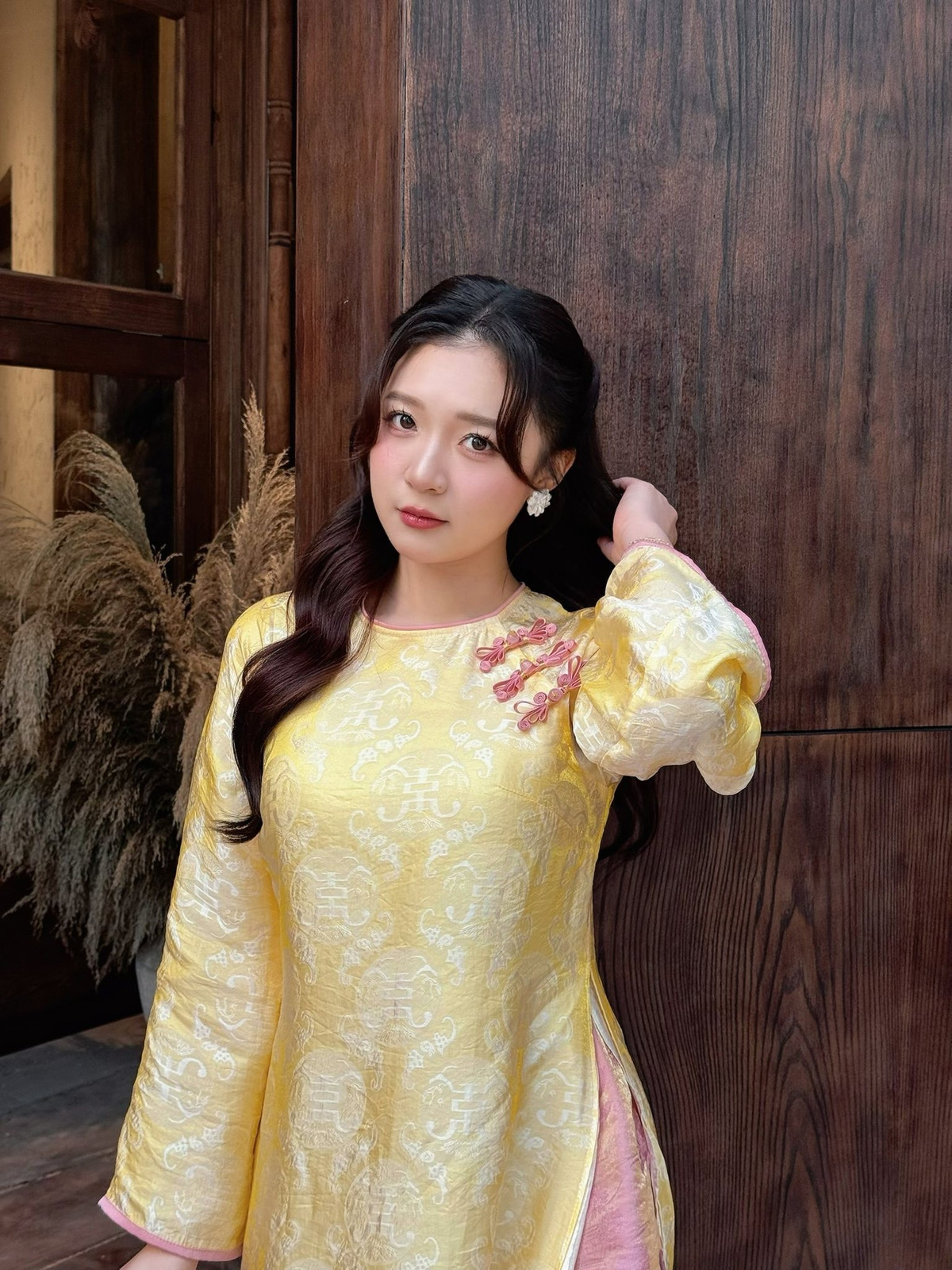 Điểm nhấn nằm ở phần cổ áo được viền hồng nhạt và những chi tiết thắt nơ nhỏ xinh trước ngực, mang đến cảm giác trẻ trung, duyên dáng đúng tinh thần ngày Tết.