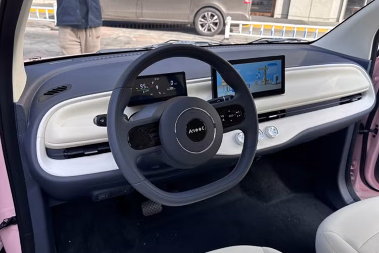 Bên trong, A100C chọn cách bố trí tối giản: màn hình cảm ứng đặt nổi trên táp-lô, cụm đồng hồ LCD riêng, và cần số đặt sau vô-lăng hai chấu. Quyết định loại bỏ khu vực bảng điều khiển trung tâm giúp tạo khoảng trống giữa hai ghế trước, tăng độ thoáng thị giác và khoảng duỗi chân – một lợi thế đáng kể trong thân xe ngắn.