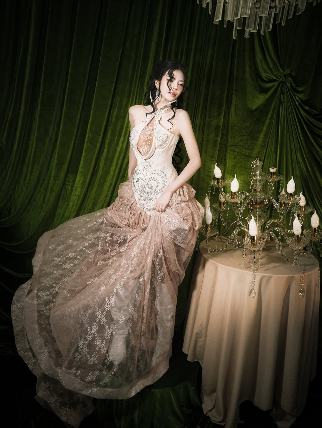 Trong bộ váy tông nude – champagne, Mai Dora khéo léo khoe đường cong mềm mại nhờ phom dáng ôm sát phần thân trên, điểm nhấn là chi tiết cắt xẻ tinh xảo và chất liệu ren, voan rủ bồng bềnh.