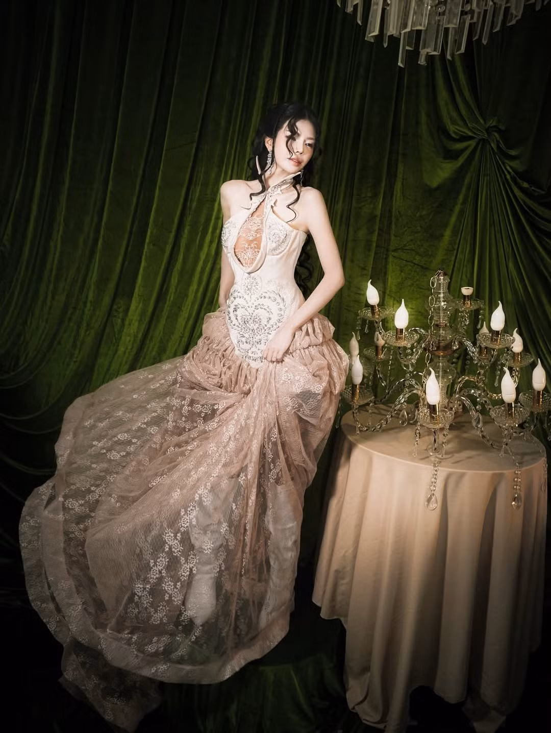 Trong bộ váy tông nude – champagne, Mai Dora khéo léo khoe đường cong mềm mại nhờ phom dáng ôm sát phần thân trên, điểm nhấn là chi tiết cắt xẻ tinh xảo và chất liệu ren, voan rủ bồng bềnh.