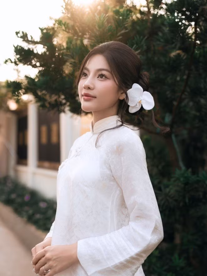 Kiểu tóc búi gọn, điểm hoa trắng sau tai cùng lớp trang điểm nhẹ giúp tổng thể ngoại hình của cô giữ được nét tinh tế, hài hòa.