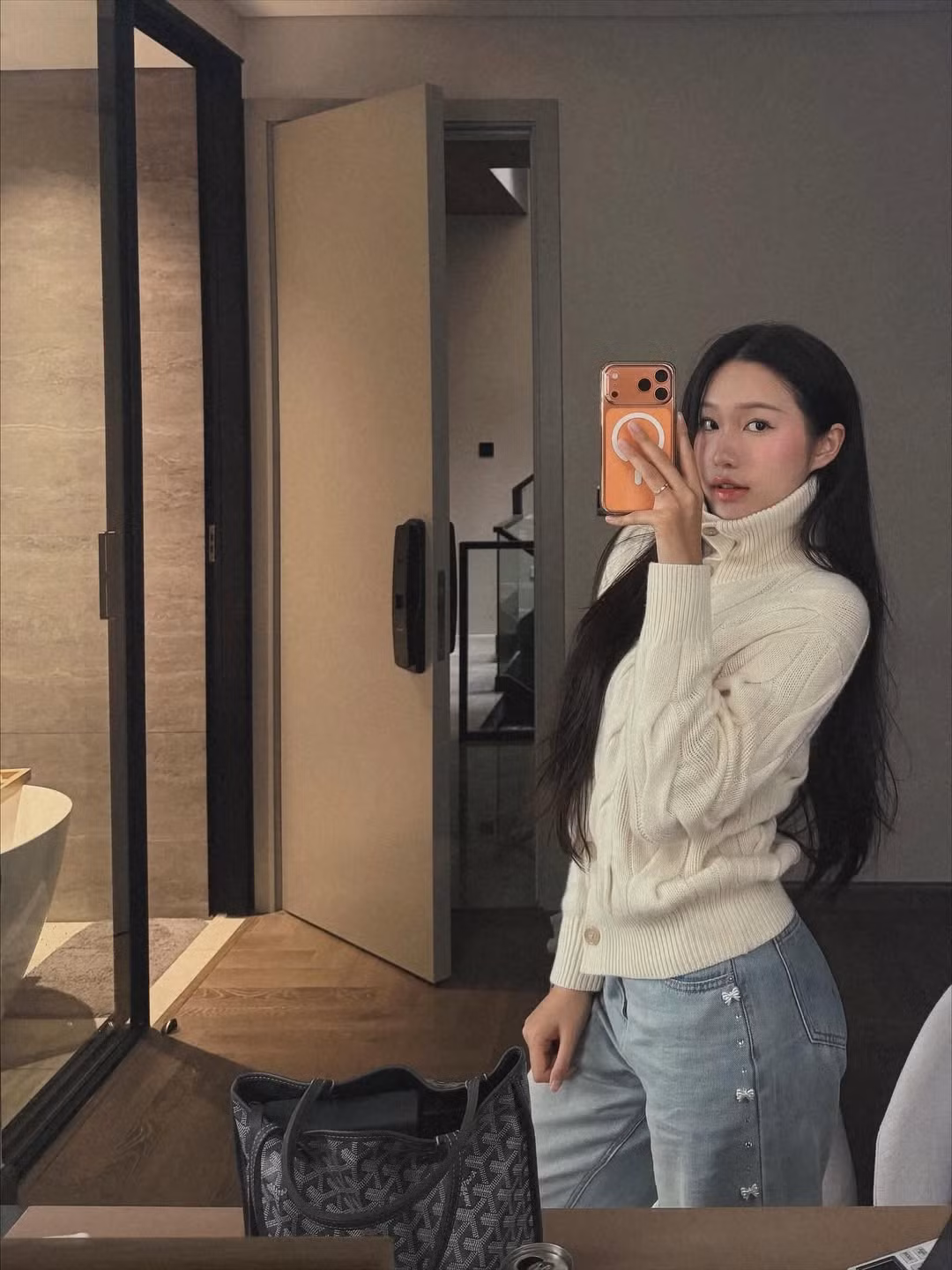 Người đẹp lựa chọn chiếc áo len cardigan màu trắng kem, có thiết kế cổ lọ cao và họa tiết đan vặn thừng (cable knit) cổ điển. Những chiếc cúc gỗ nhỏ xinh xắn trên áo càng tăng thêm vẻ ngọt ngào, ấm áp cho tổng thể.