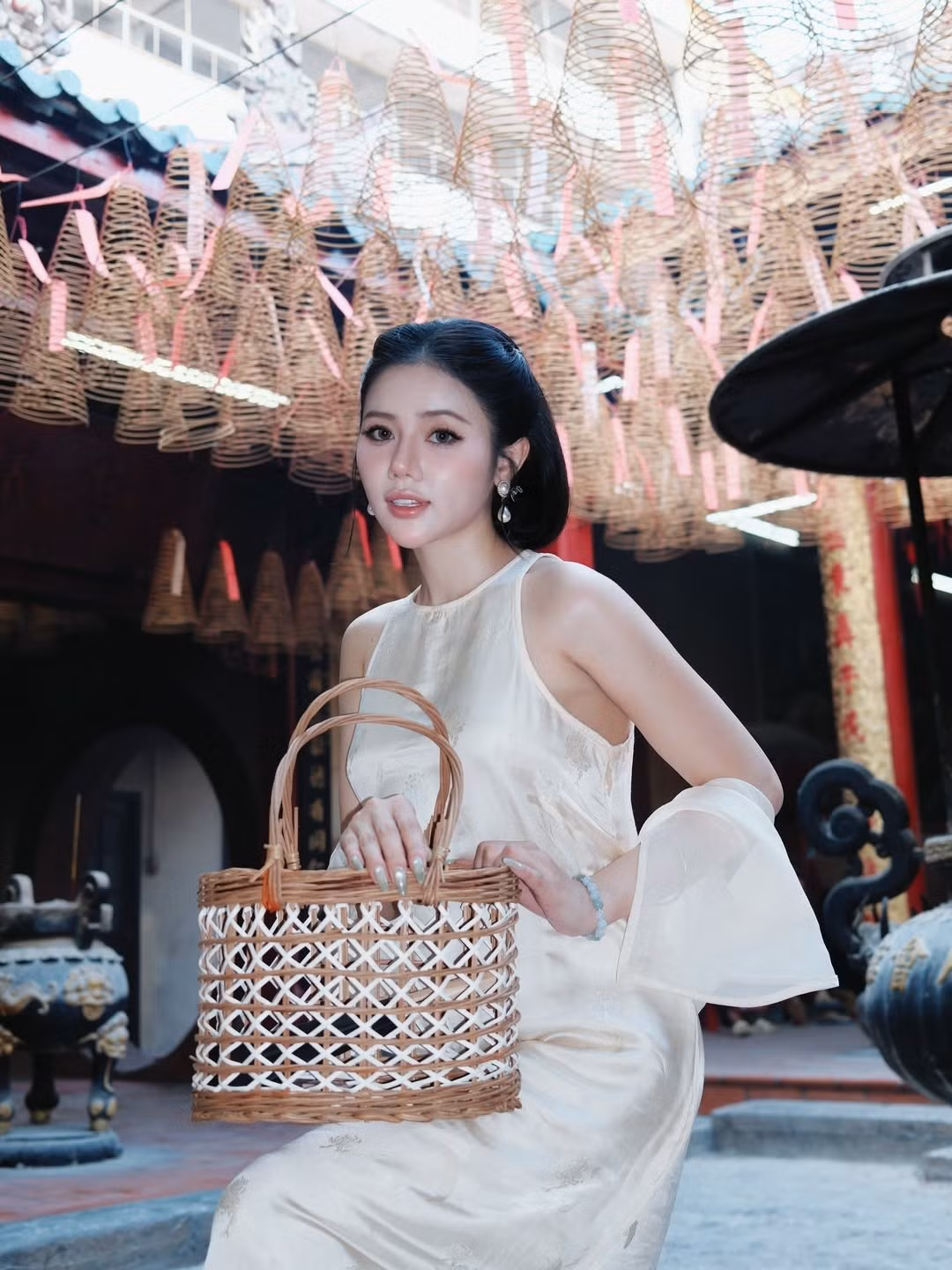 Trong loạt ảnh mới chia sẻ trên mạng xã hội, Bò Chảnh lựa chọn phong cách kín đáo nhưng vẫn tôn lên vẻ nữ tính. Thiết kế áo lụa suông nhẹ, chất vải mềm rủ tự nhiên giúp cô toát lên hình ảnh thanh lịch, nền nã. Gam màu trắng kem không chỉ tôn da mà còn hòa hợp với bối cảnh cổ kính của khu phố người Hoa – nơi nổi tiếng với những mái ngói cong, họa tiết rồng phượng và đèn lồng đỏ treo cao.