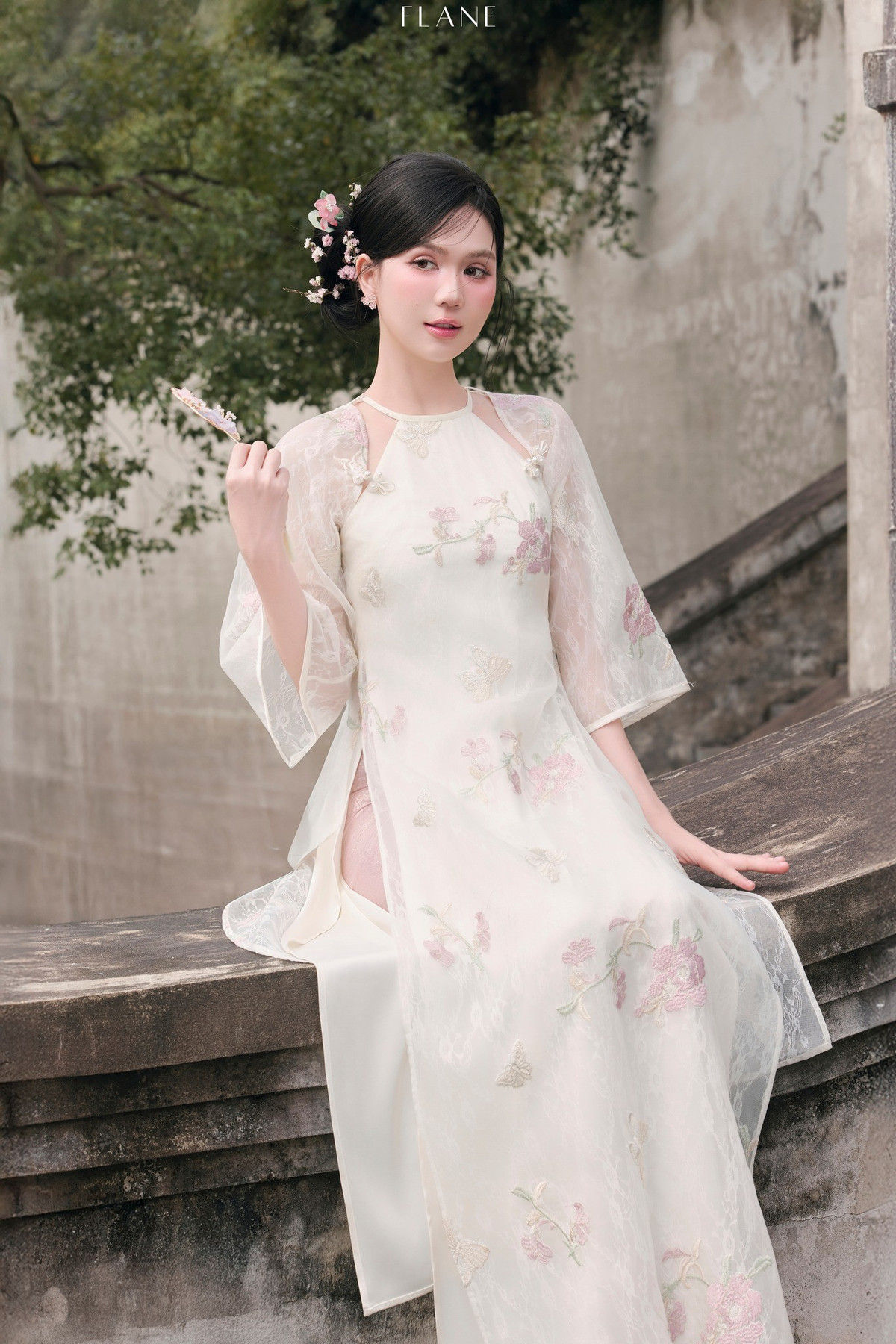 Trong loạt ảnh mới đây, Ngọc Trinh diện tà áo dài tông trắng ngà, điểm họa tiết hoa thêu pastel, giúp tôn lên vẻ mềm mại, nền nã và nữ tính của người đẹp Trà Vinh.