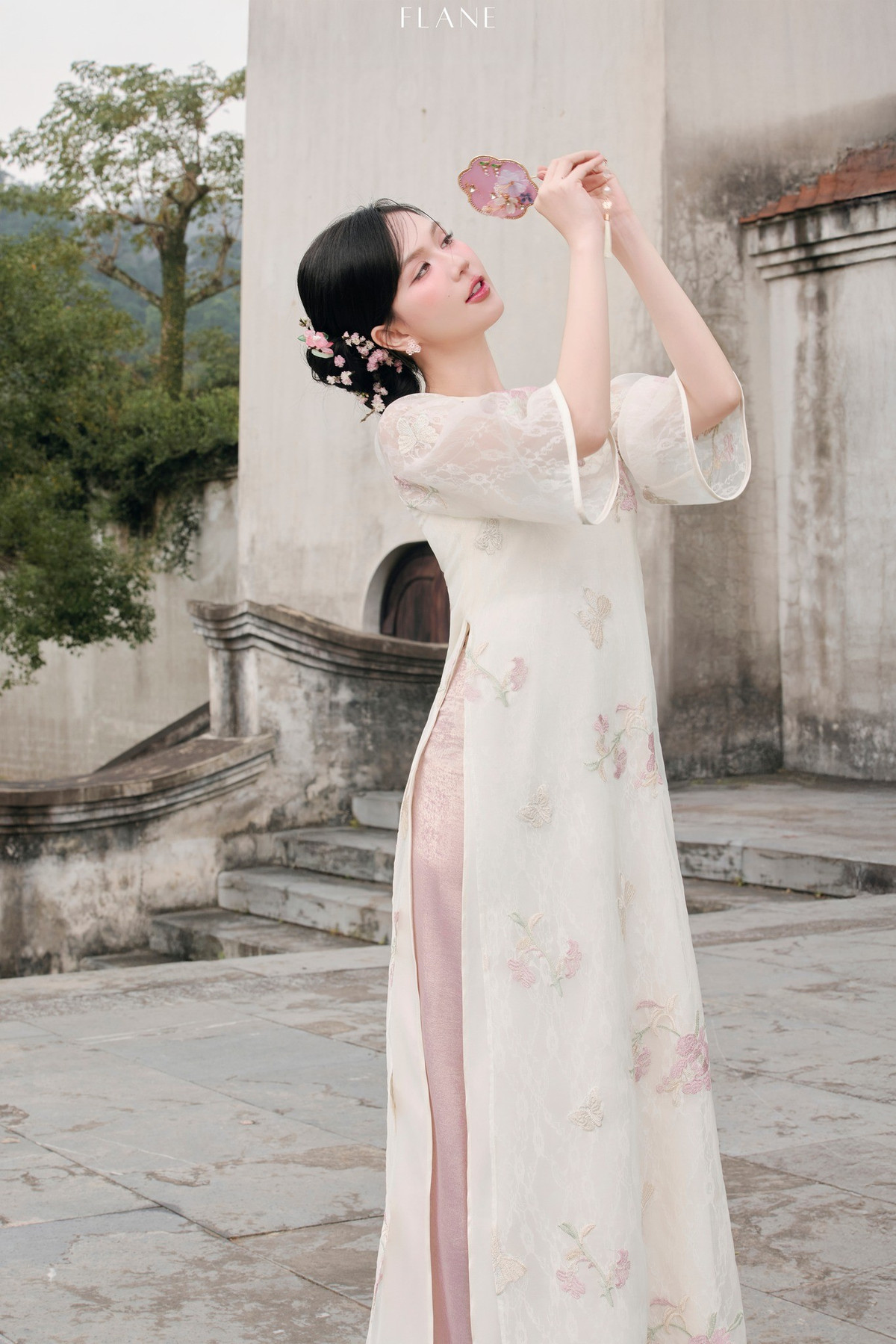 Kiểu tóc búi thấp, cài hoa nhỏ phía sau càng tăng vẻ cổ điển, khiến Ngọc Trinh trông như bước ra từ một bức tranh xưa.