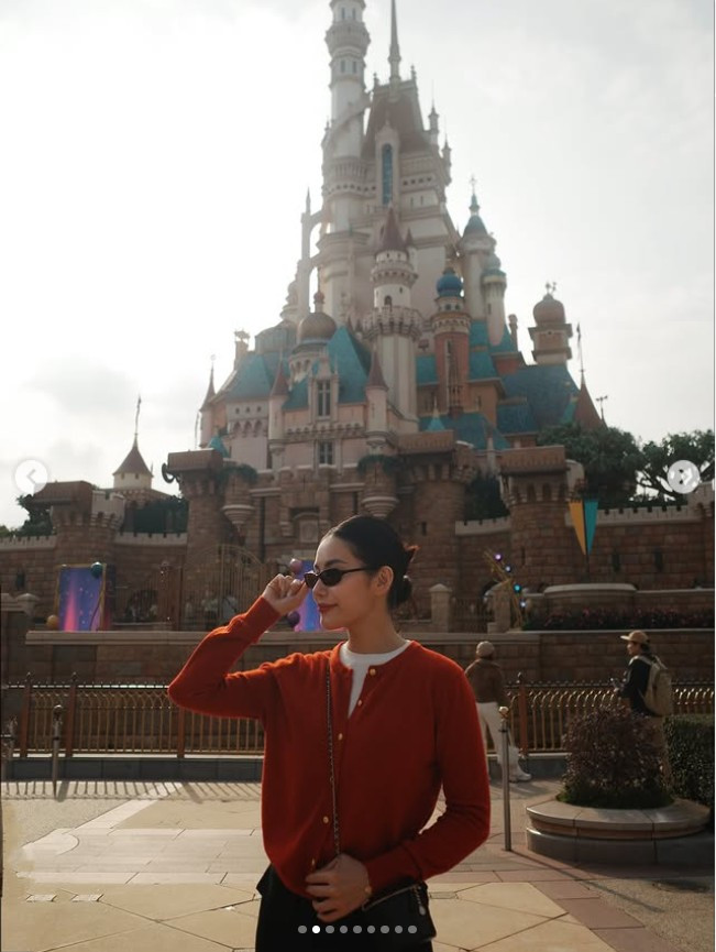 Không chỉ dạo phố, Milan Phạm còn ghi lại những khoảnh khắc check-in tại Hong Kong Disneyland. Diện cardigan đỏ nổi bật phối cùng chân váy ngắn, cô mang đến hình ảnh trẻ trung, tươi tắn nhưng vẫn giữ được nét thanh lịch.