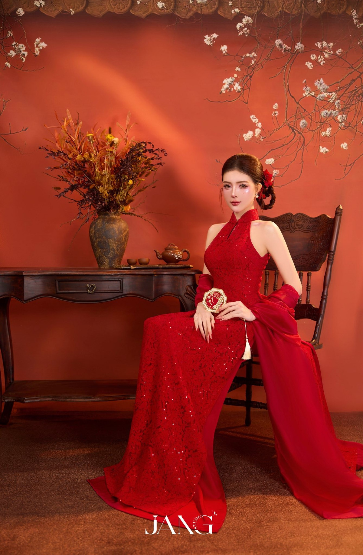 Phom dáng mềm mại kết hợp chất liệu ren và sequin tinh tế giúp tôn trọn đường cong cơ thể, đồng thời làm nổi bật nét nữ tính, quyến rũ nhưng vẫn giữ được sự thanh lịch. Chiếc khăn choàng đỏ buông nhẹ trên tay càng tăng thêm vẻ thướt tha, đậm chất Á Đông.