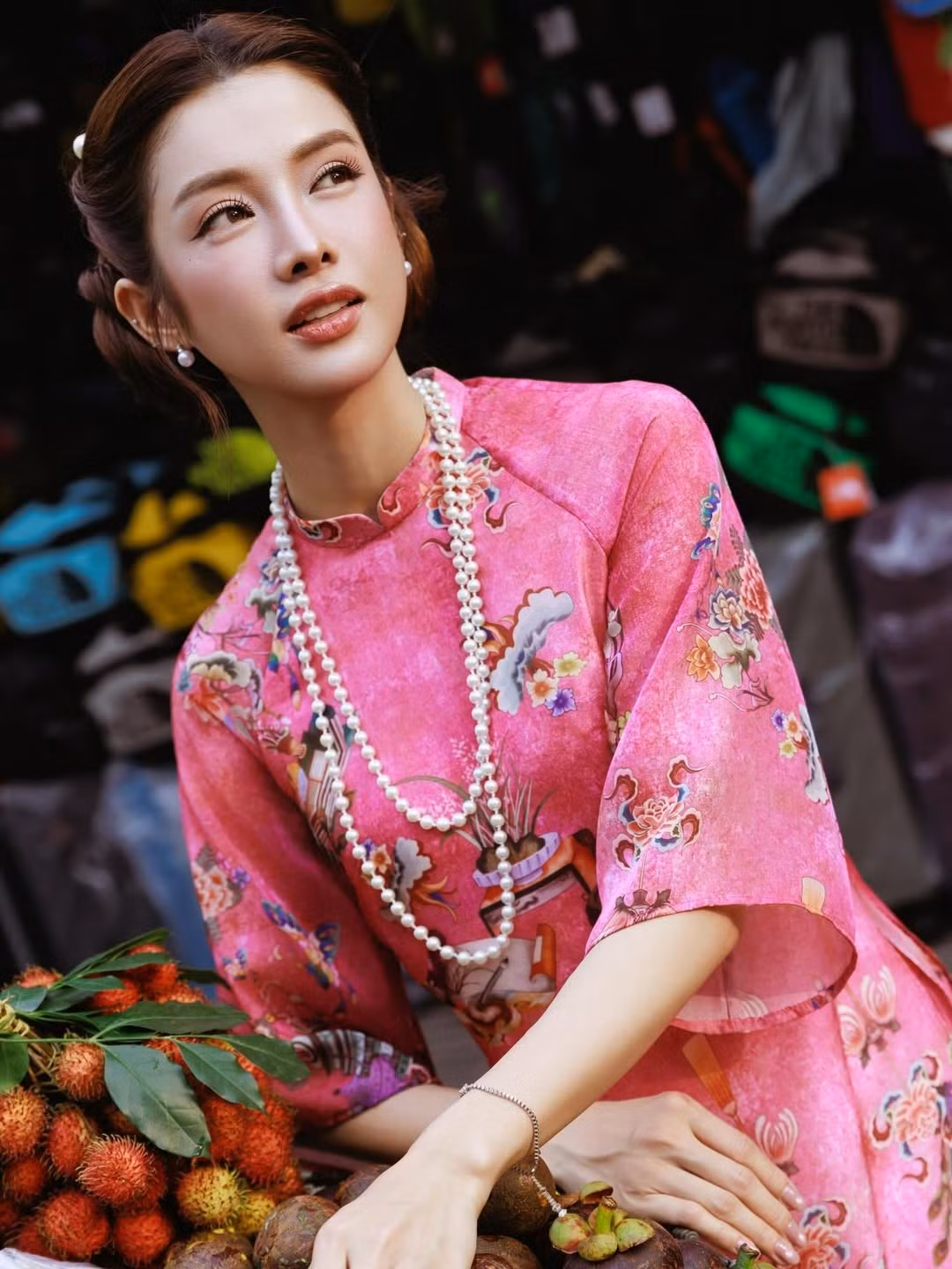 Điểm thú vị của bộ ảnh của Mỹ Duyên nằm ở bối cảnh rất đời: sạp trái cây, quán ăn bình dân, bảng hiệu cũ kỹ, xe máy đậu sát lề đường. Những khung hình được ghi lại gần khu vực Chợ Bến Thành mang đậm chất Sài Gòn – nơi quá khứ và hiện tại luôn song hành. Giữa không gian đó, tà áo dài của nữ diễn viên thướt tha bay nhẹ theo từng bước chân tạo nên sự đối lập đầy thi vị: truyền thống giữa nhịp sống hiện đại.