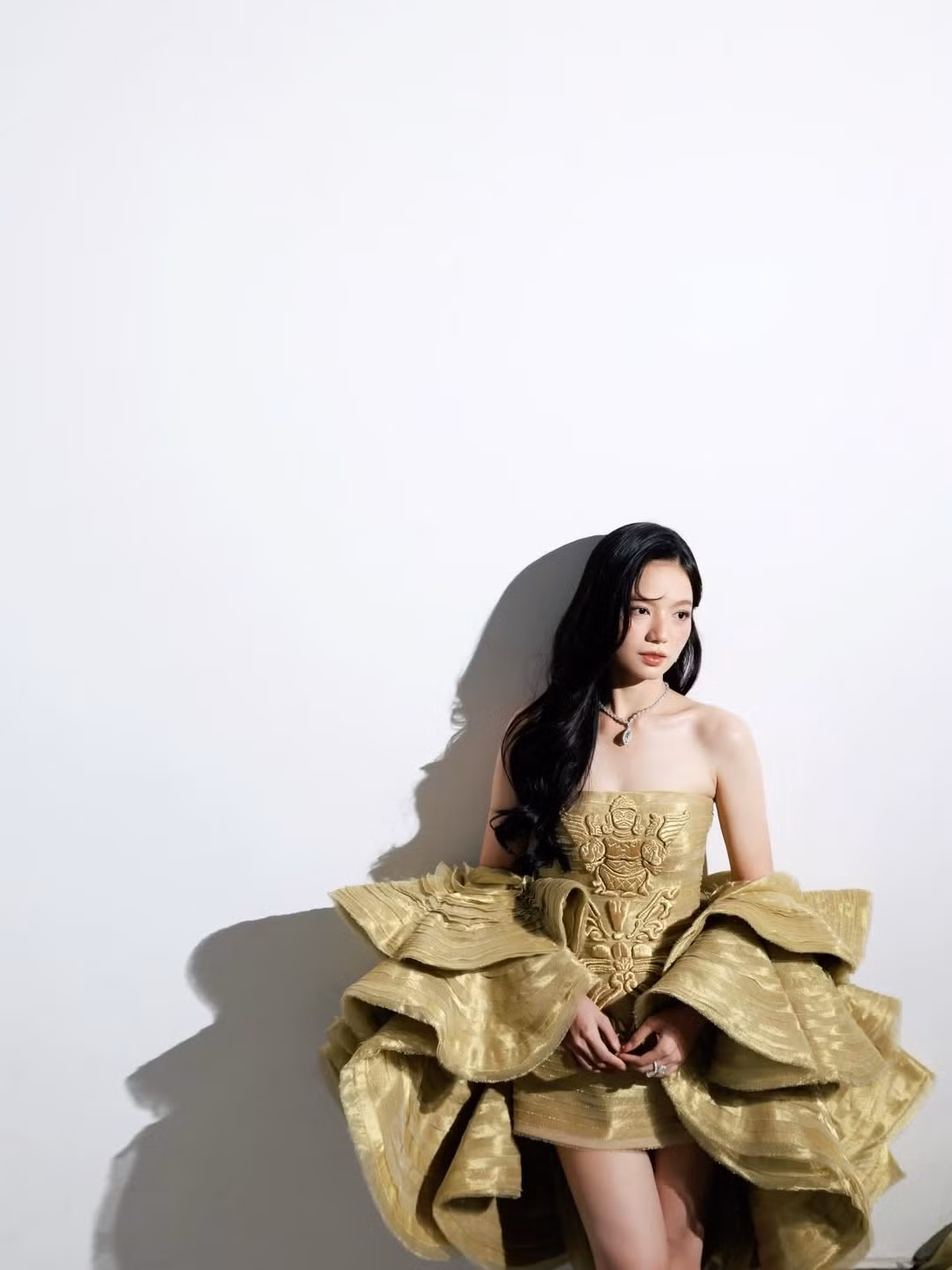 Bộ trang phục được Hạ Anh lựa chọn có thiết kế cầu kỳ và hoàn toàn nổi bật. Đầm vàng ánh kim với họa tiết thêu nổi tinh xảo, tạo điểm nhấn hoàng gia. Phần tay áo phồng xếp lớp mang lại cảm giác lộng lẫy như bước ra từ một buổi dạ hội.
