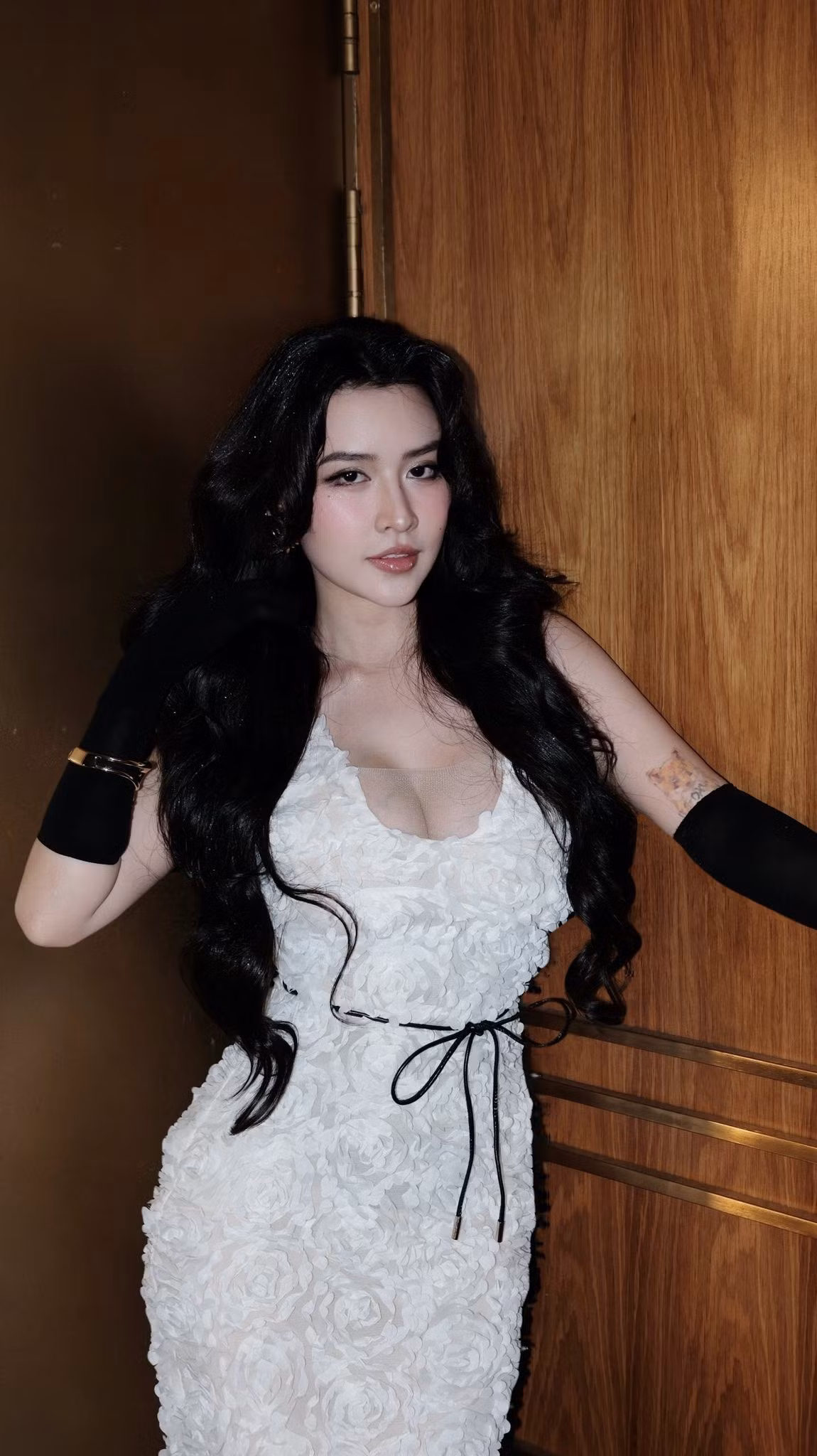 Làn da trắng mịn, gương mặt V-line cùng đôi môi hồng căng bóng mang lại vẻ đẹp vừa ngọt ngào vừa sắc sảo. Mái tóc đen uốn lọn dài buông nhẹ tạo cảm giác cổ điển, sang trọng, gợi nhớ hình ảnh các minh tinh châu Á thập niên 90.