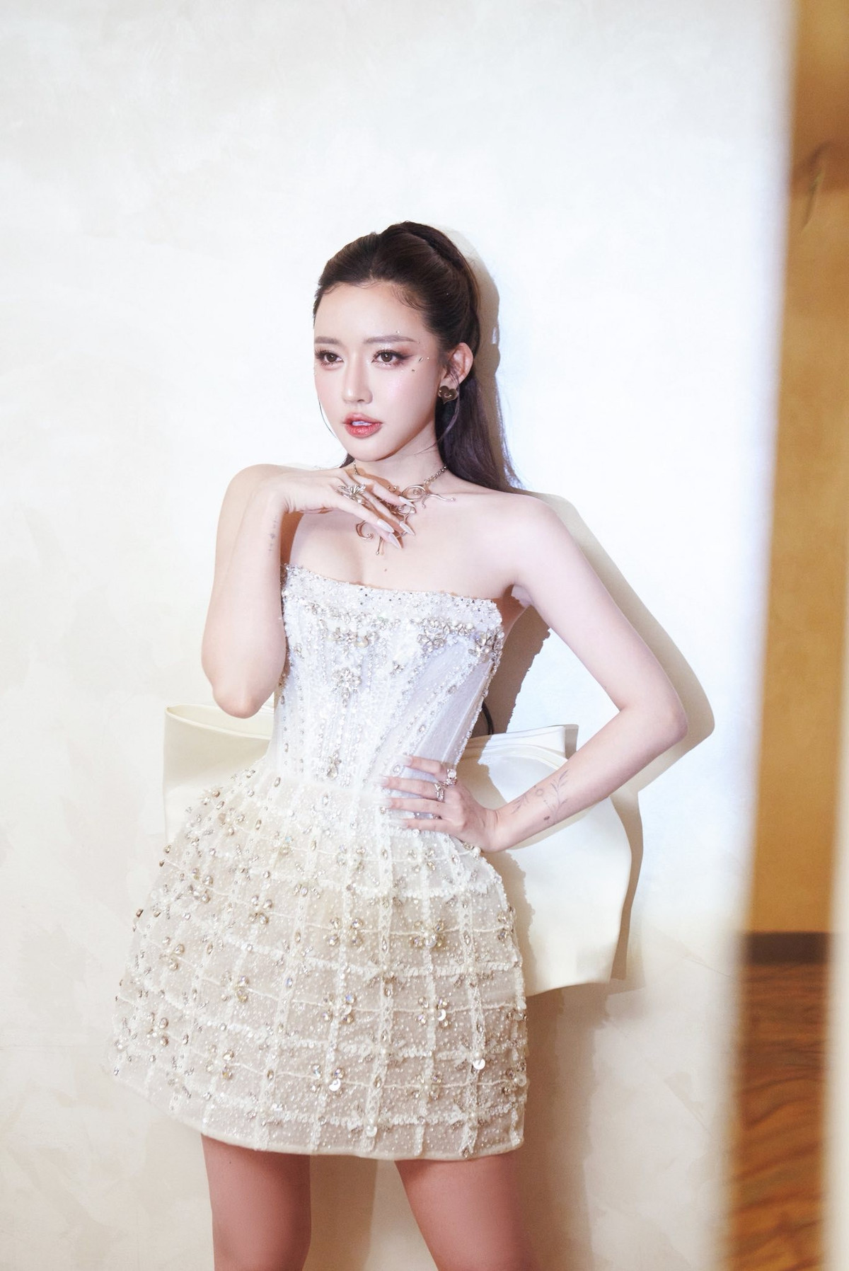 Diện chiếc đầm ngắn corset trắng đính kết cầu kỳ, phủ lấp lánh hàng trăm chi tiết pha lê và sequin, Bích Phương trông vô cùng nổi bật. Thiết kế với phom dáng ôm sát phần thân trên, xòe nhẹ ở chân váy tôn đường cong mềm mại, mang đến cảm giác sang trọng nhưng vẫn trẻ trung. Phần nơ lớn phía sau tạo hiệu ứng thị giác như một nàng công chúa bước ra từ buổi tiệc xa hoa.