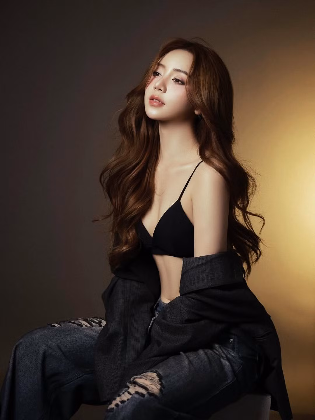 Tone màu tối của trang phục kết hợp ánh sáng vàng ấm phía sau tạo hiệu ứng tương phản, giúp Quỳnh Kool nổi bật với thần thái sắc sảo và phong cách thời trang trưởng thành.