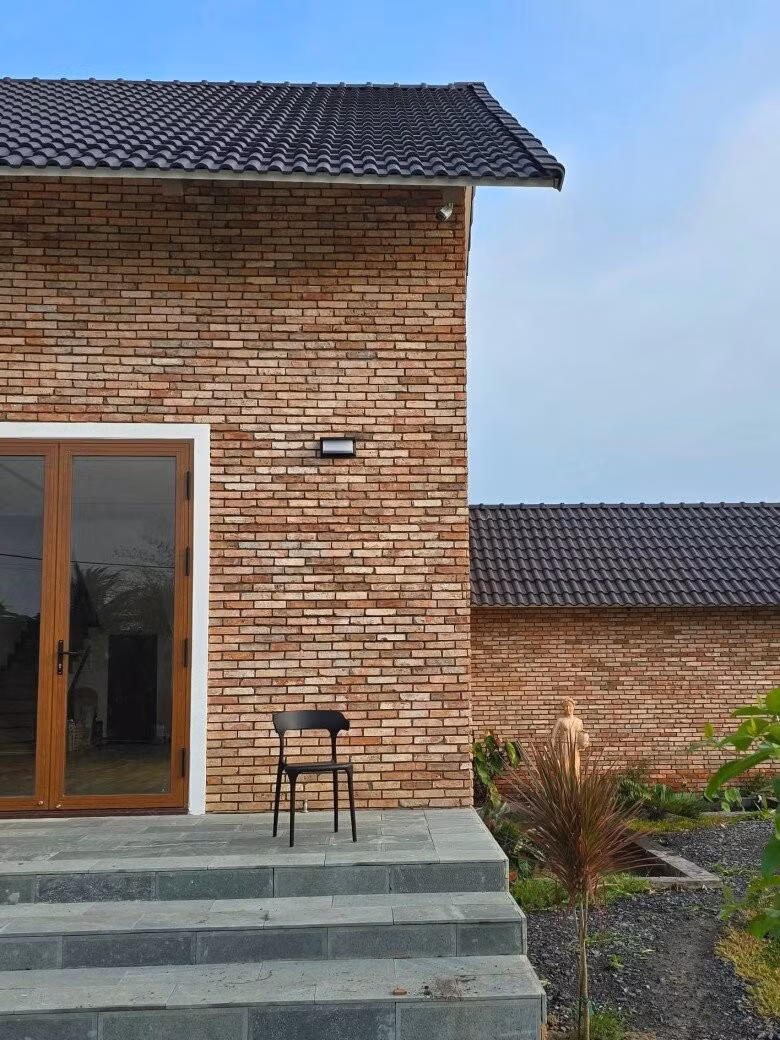 Ngôi nhà chính thiết kế theo phong cách hiện đại nhưng vẫn giữ nét mộc mạc nhờ mảng tường gạch trần không tô trát. Ảnh: FBNV