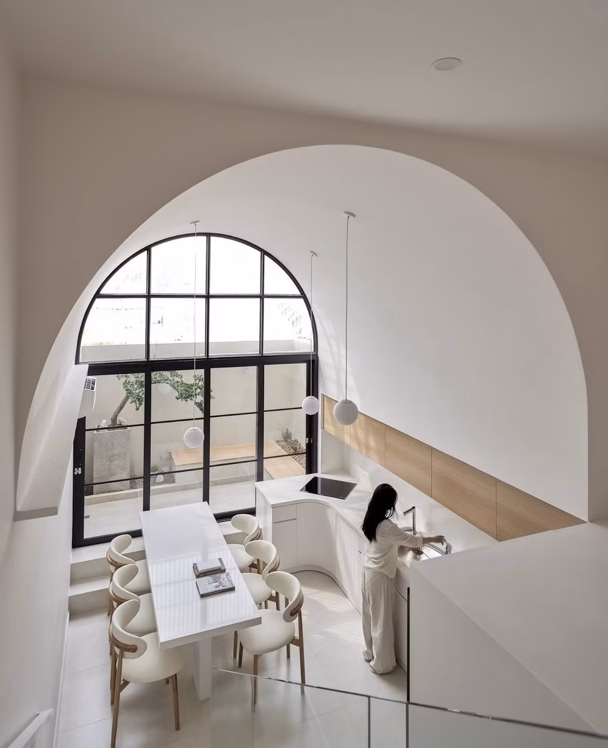 Trong khi nhiều nhà phố đặt phòng khách làm trung tâm, thì White Oasis tái định vị bếp và bàn ăn thành “linh hồn” của công trình. Một khoảng vòm cao xuyên tầng được mở ra, kết hợp bề mặt kính lớn giúp ánh sáng tràn ngập không gian. Ảnh: Phú Đào