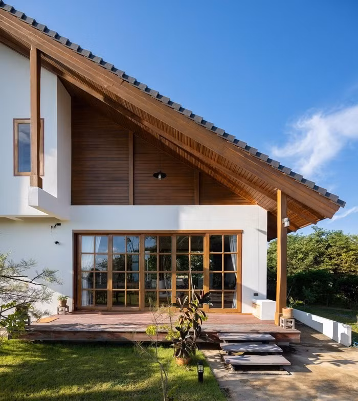 Mái dốc kết hợp trần hiên ốp gỗ tạo lớp vỏ mềm mại cho mặt tiền. Ảnh: Rungkit Charoenwat